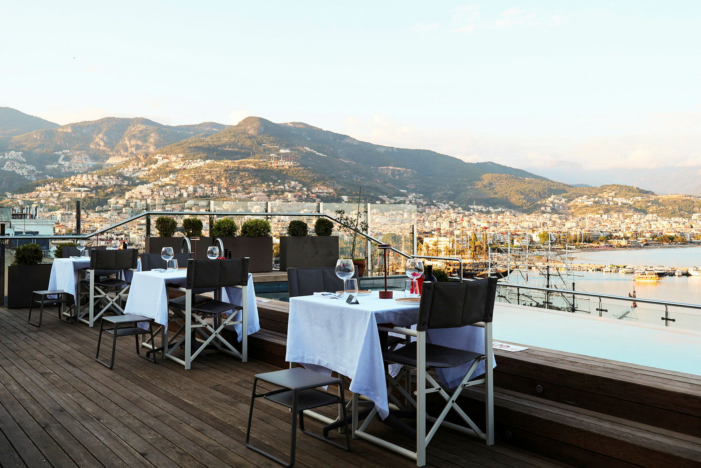 Restaurantborde på en terrasse med udsigt over bjerge og hav. (AI-genereret tekst)