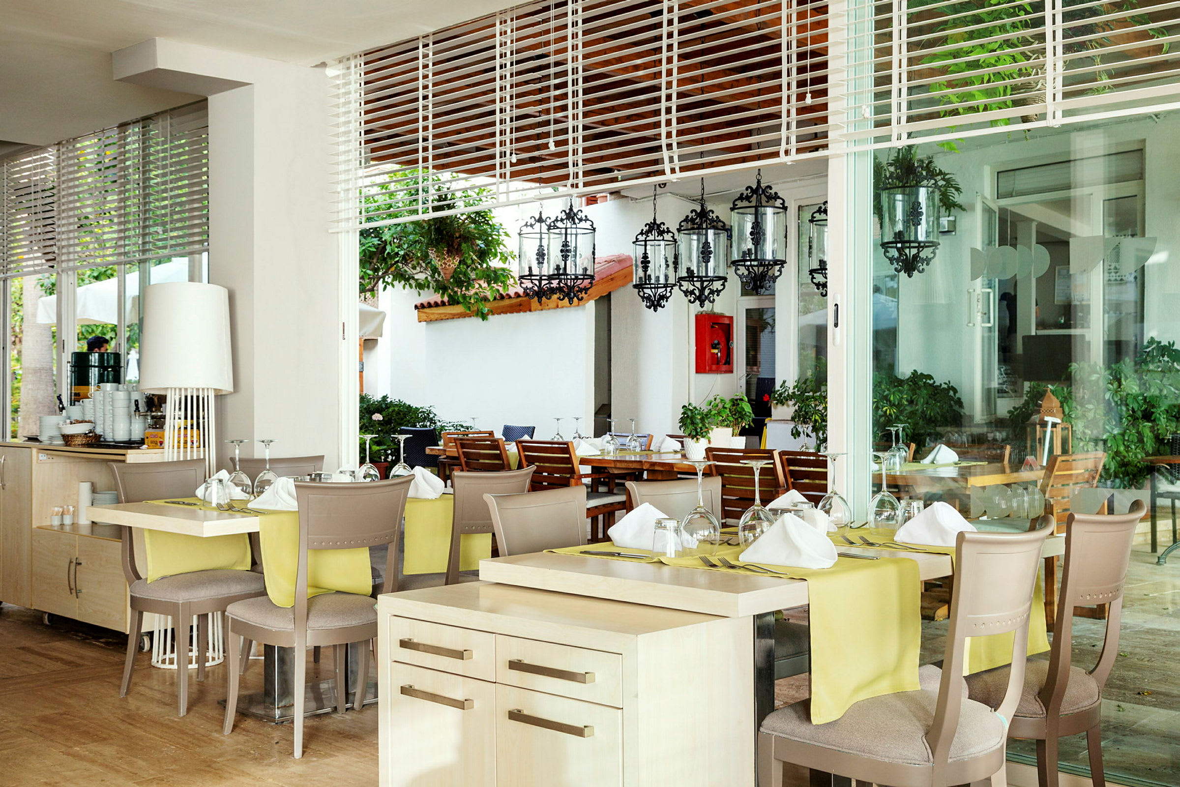 Restaurant med dækkede borde og glasudsigt mod en terrasse med stole og planter. (AI-genereret tekst)