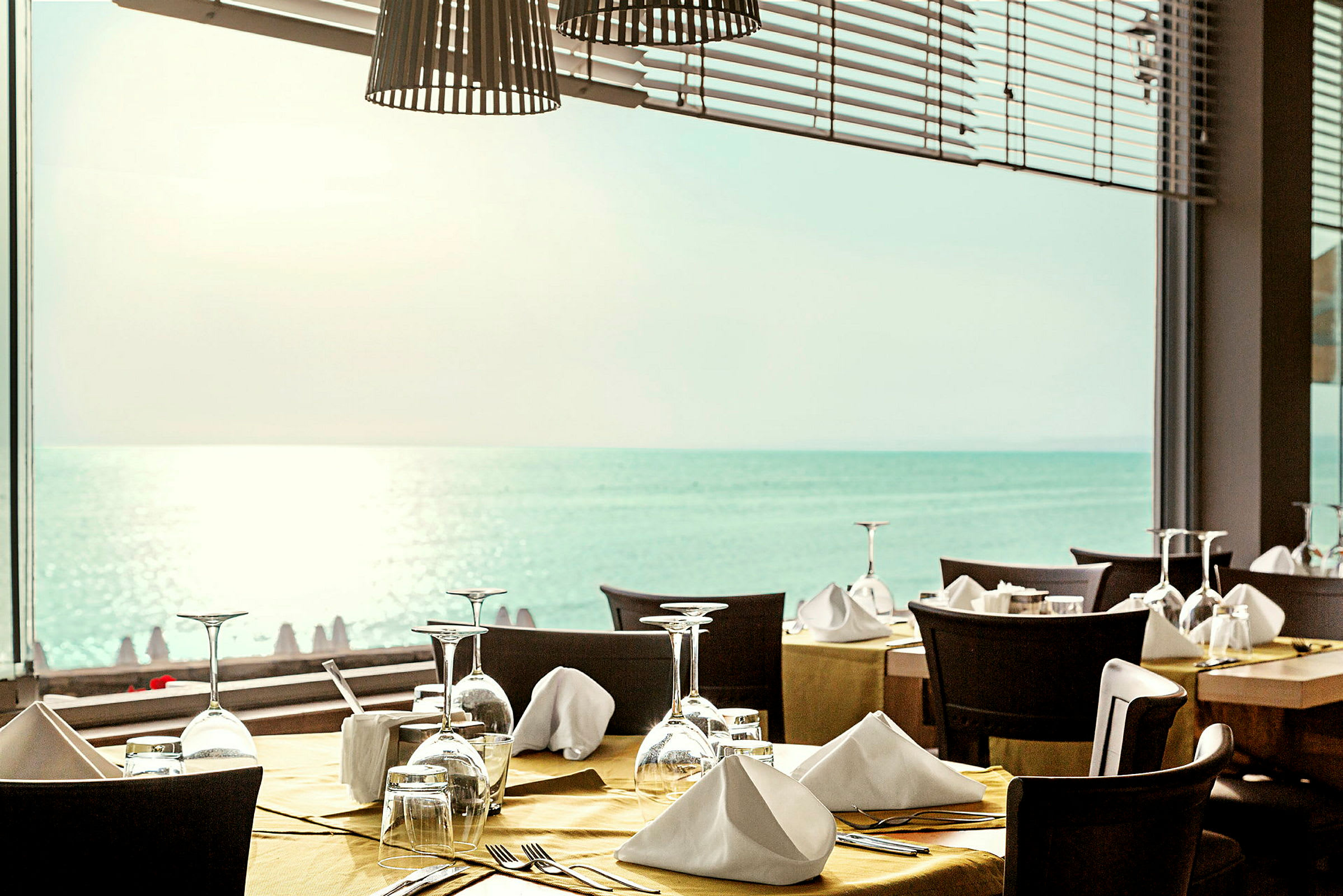 Restaurant med dækkede borde foran et vindue med udsigt over havet. (AI-genereret tekst)