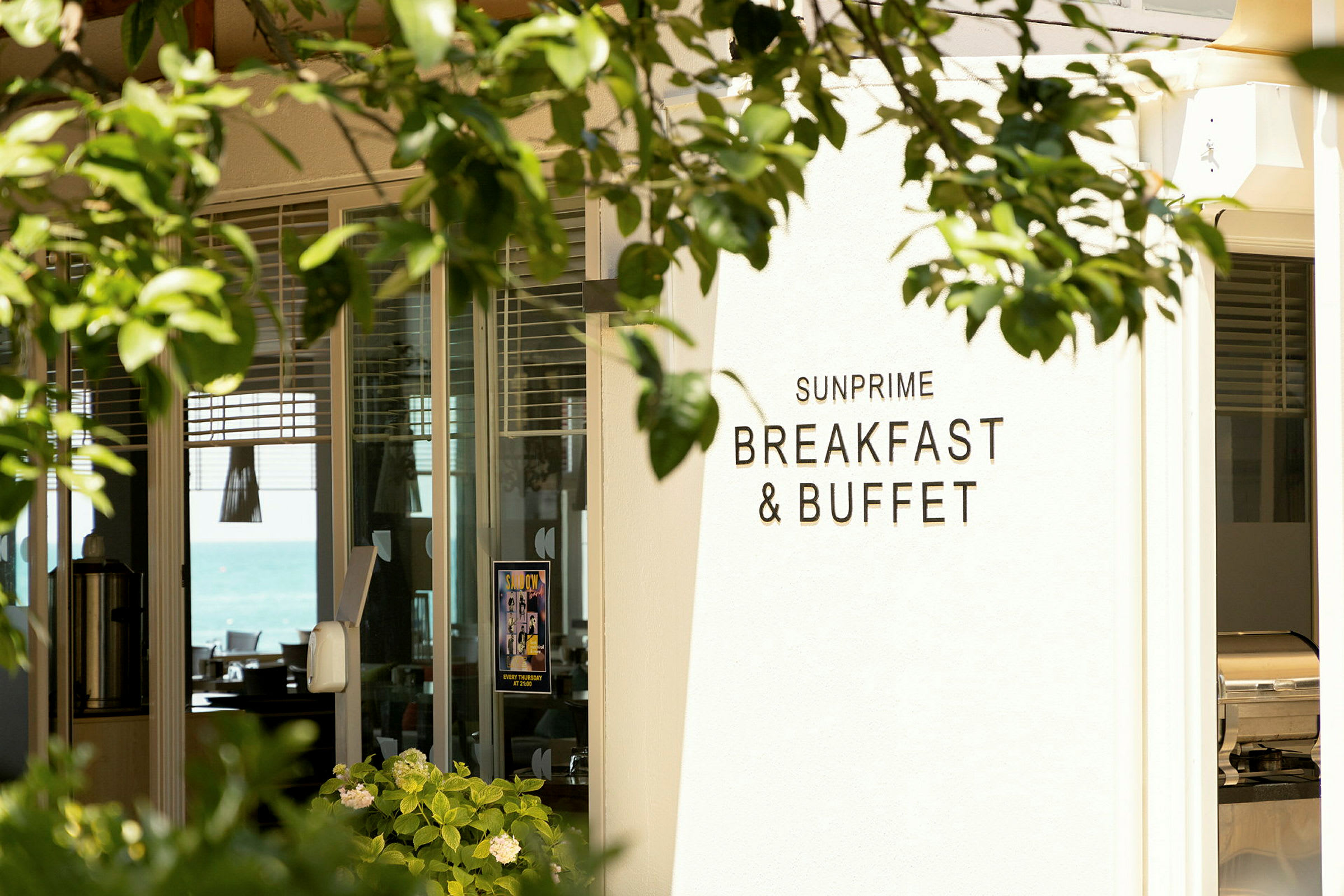 Skilt med teksten 'Sunprime Breakfast & Buffet' ved indgangen til en restaurant, omgivet af grønt. (AI-genereret tekst)