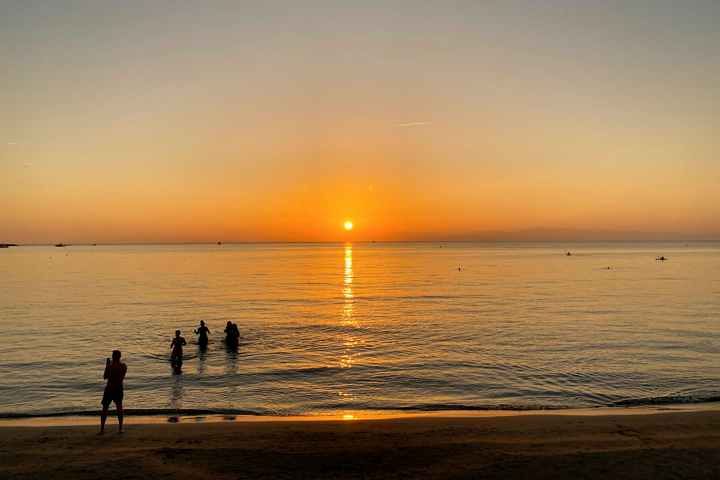 En strand ved solnedgang med mennesker i vandet. (AI-genereret tekst)