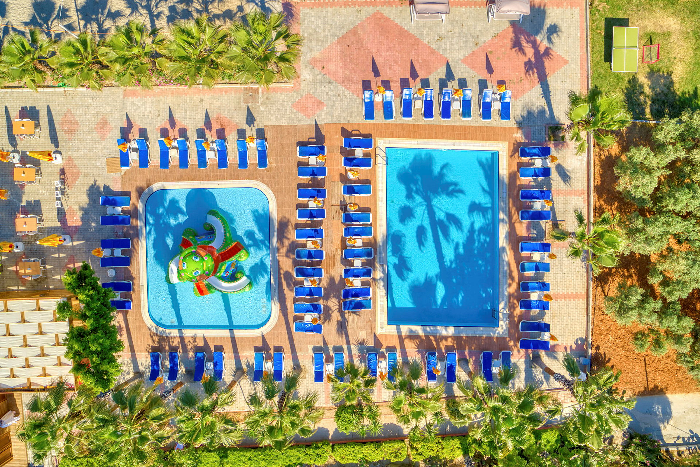 Luftfoto af en udendørs pool med liggestole rundt om og en børnepool med vandlege. (AI-genereret tekst)