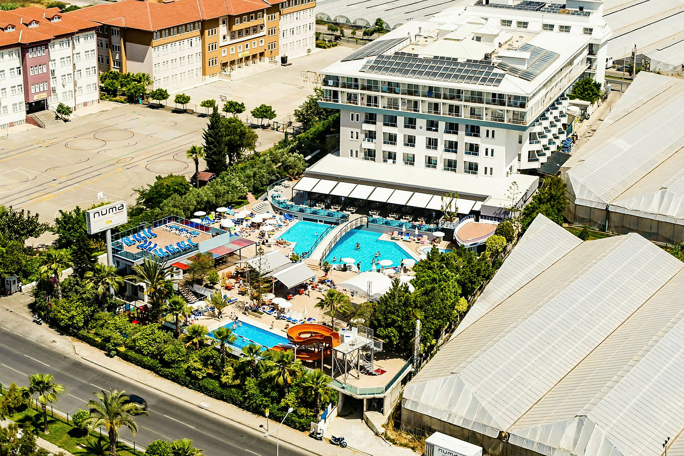 Luftfoto af et hotel med udendørs swimmingpools og omkringliggende bygninger. (AI-genereret tekst)