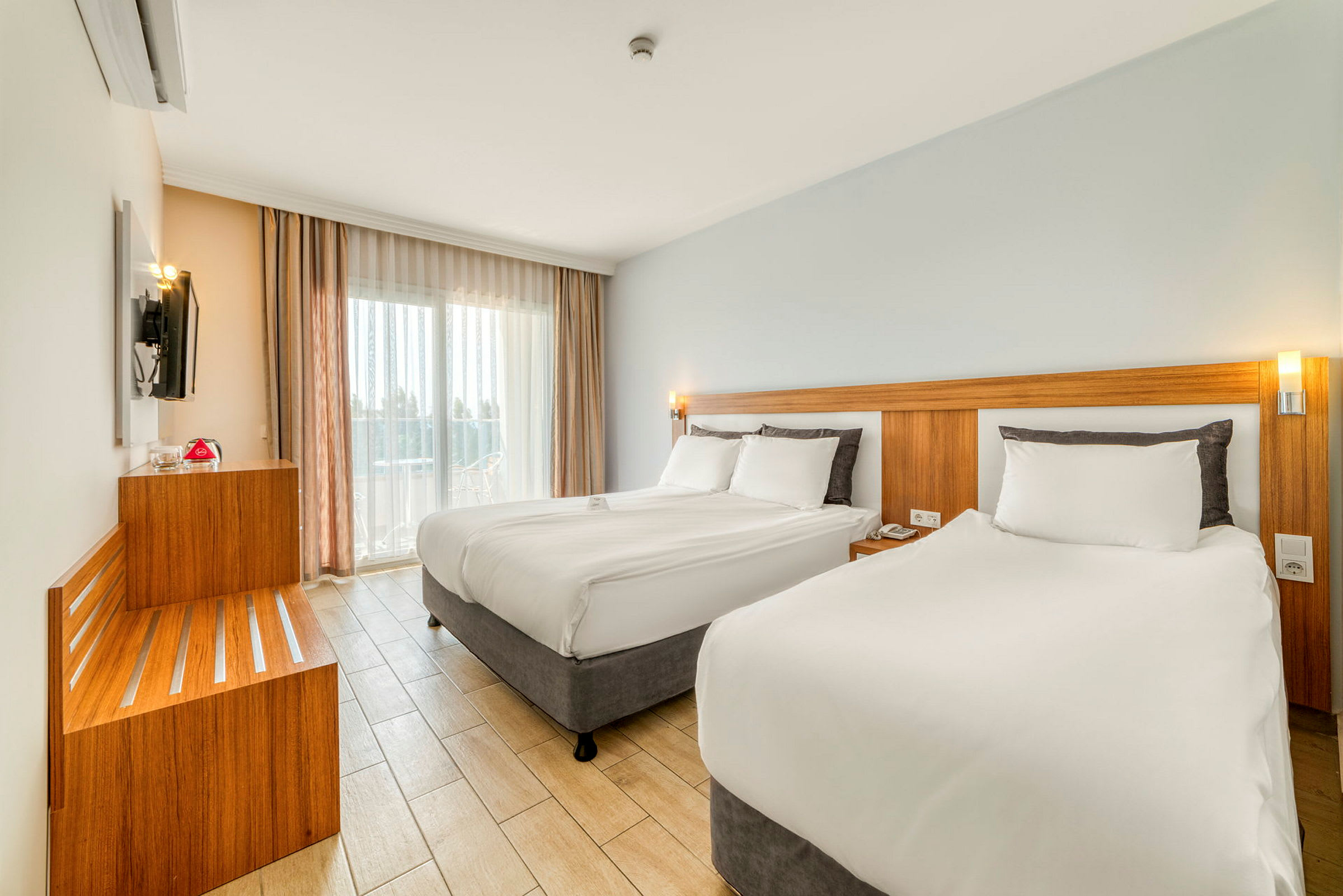 Moderne hotelværelse med to senge, lyse farver og store vinduer. (AI-genereret tekst)