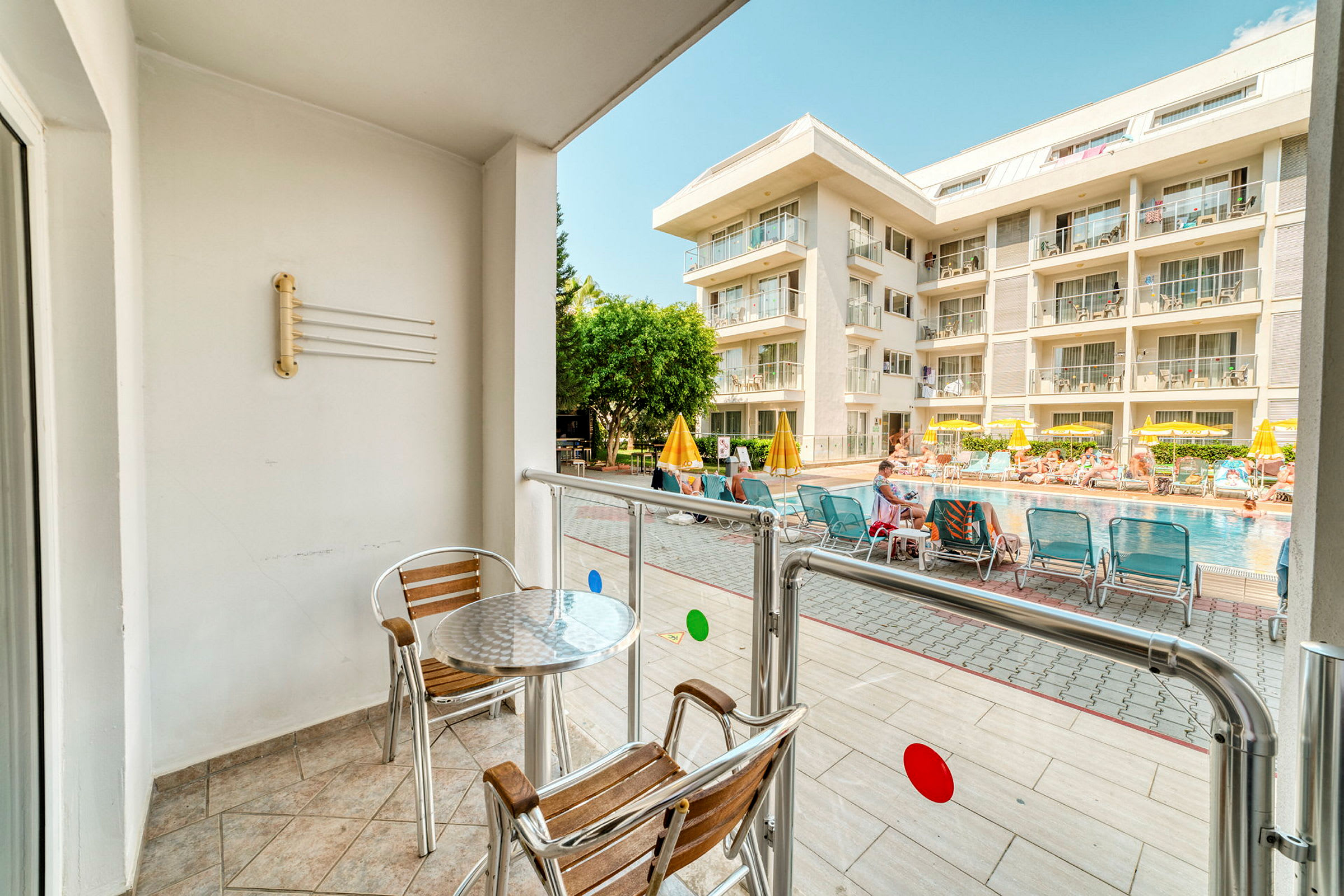 En balkon med bord og stole vender mod en pool og et hotel. (AI-genereret tekst)