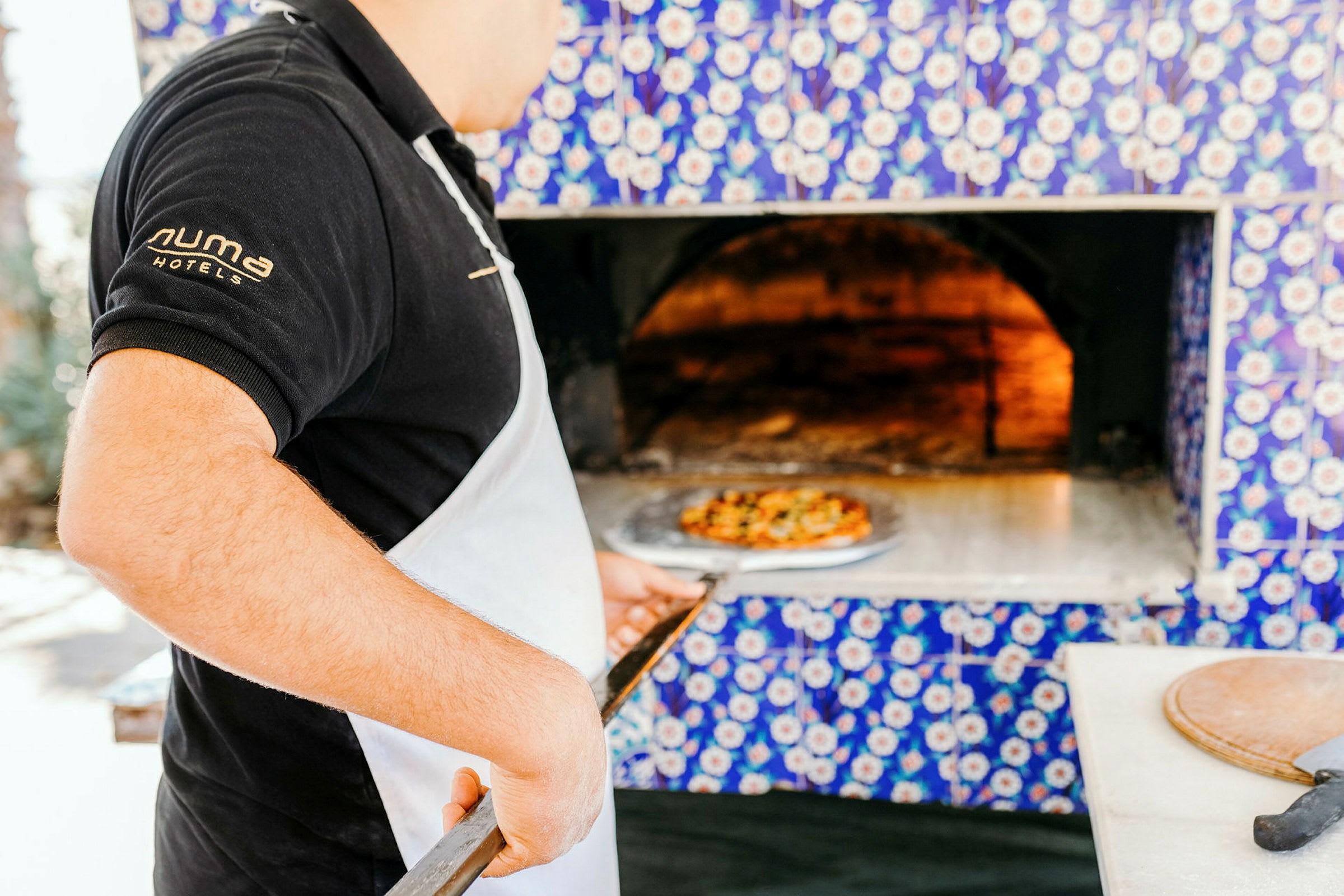 Person holder en pizzaspade foran en brændeovn. (AI-genereret tekst)