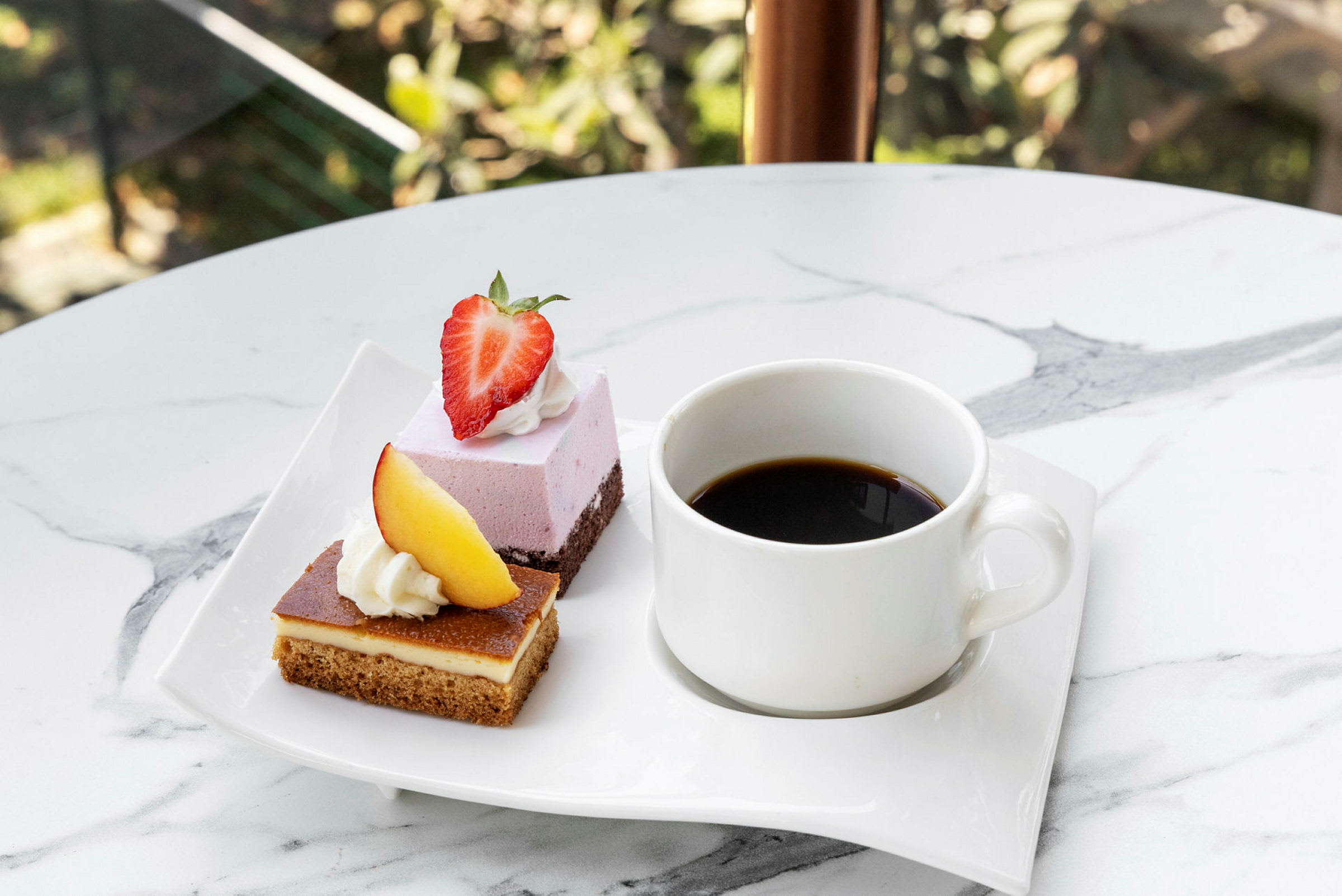 En hvid tallerken med to desserter, den ene toppet med et jordbær og den anden med et stykke fersken, samt en kop sort kaffe. (AI-genereret tekst)