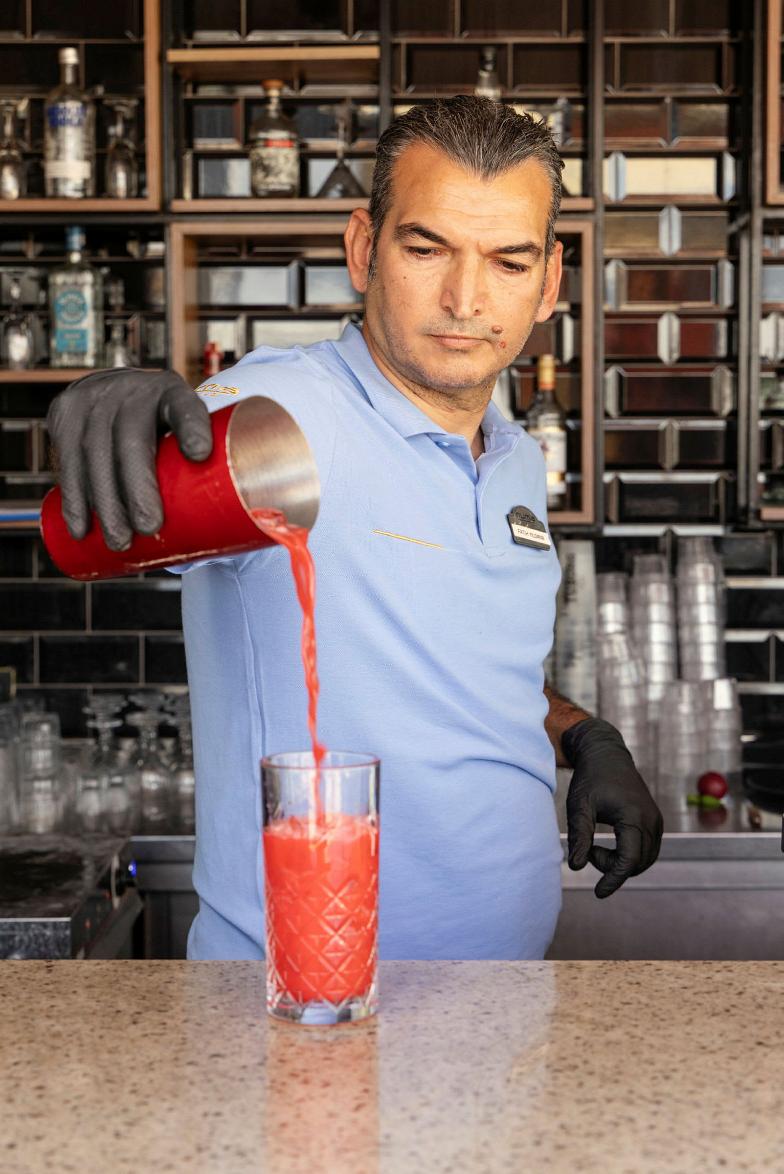 En bartender hælder en rød drik fra en shaker i et glas. (AI-genereret tekst)