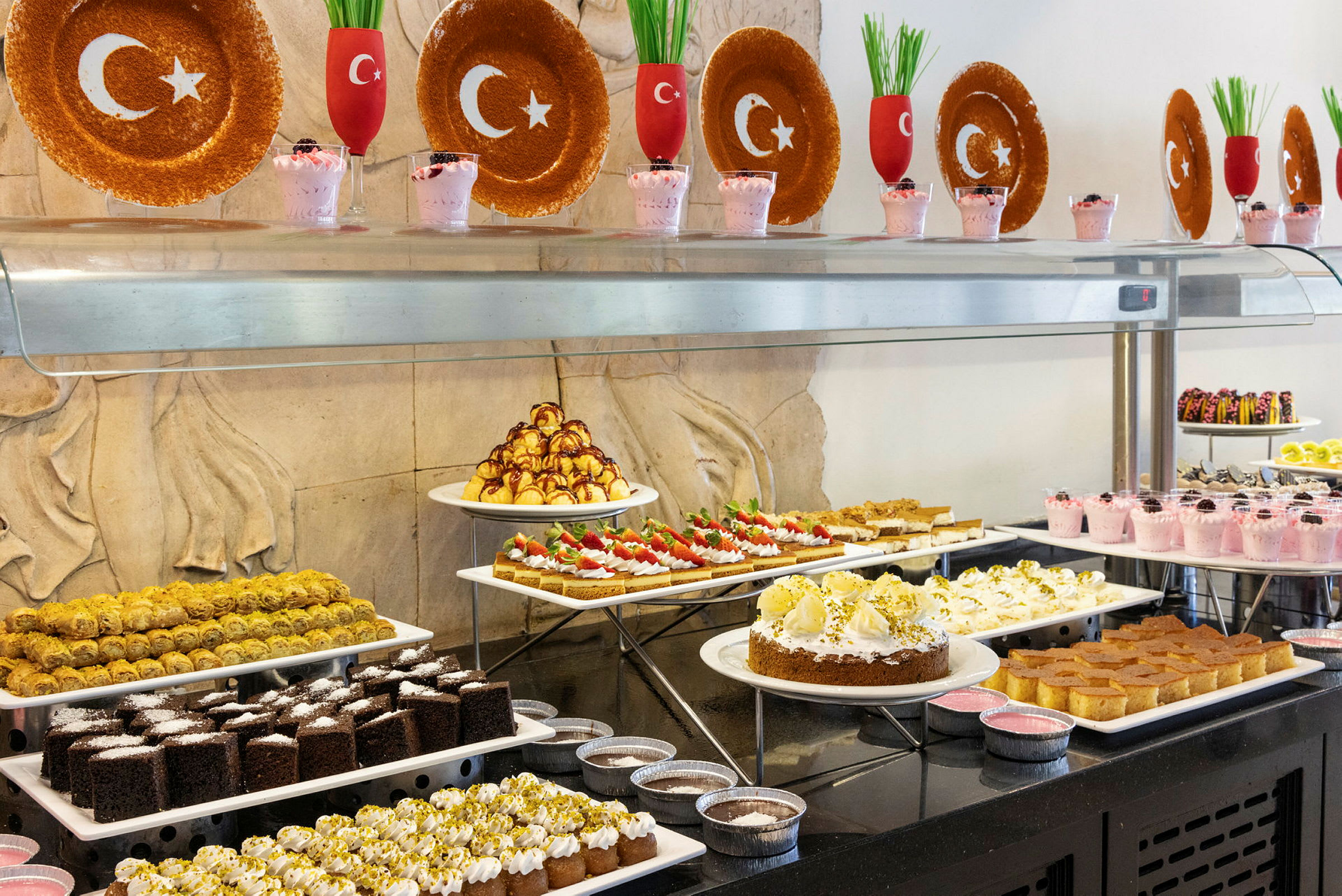 Billede af en dessertbuffet med forskellige bagværk og desserter, dekoreret med tallerkener og glas med tyrkiske flagsymboler. (AI-genereret tekst)