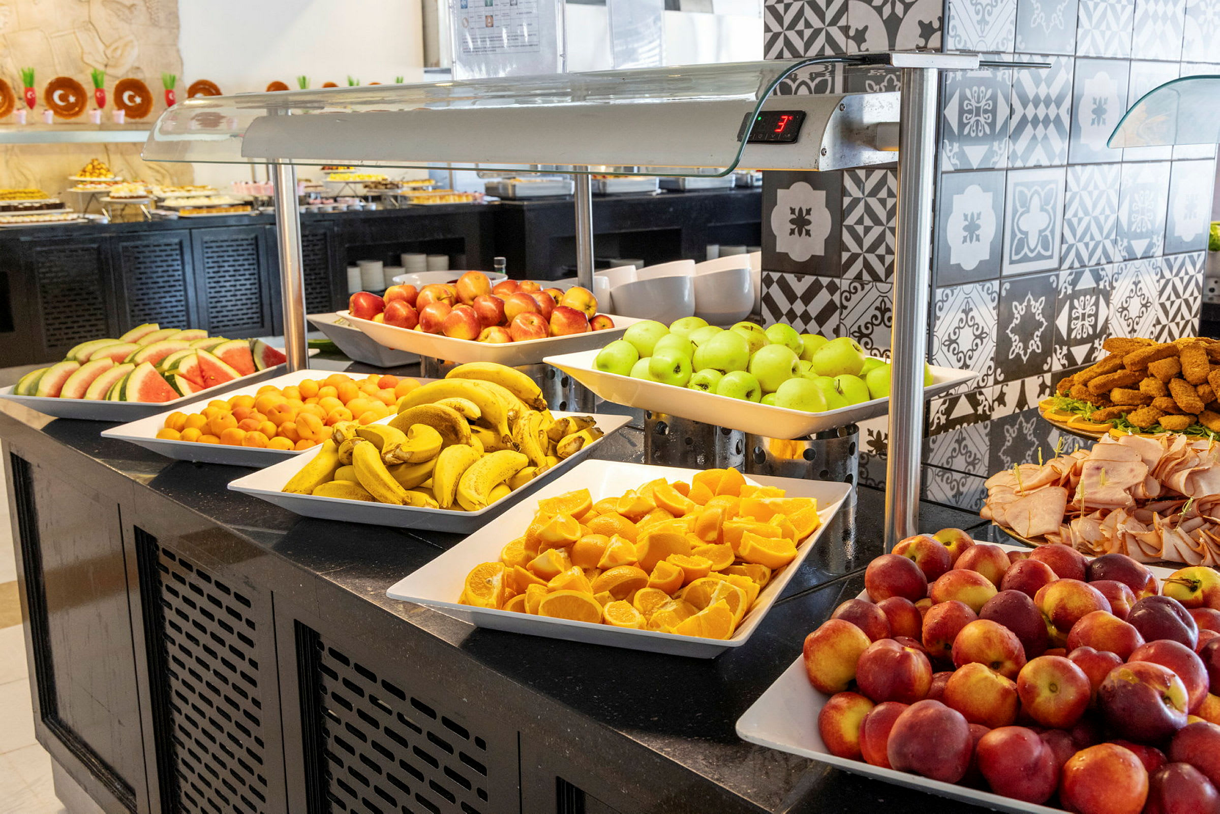 En buffet med forskellige frugter såsom bananer, æbler, appelsiner og vandmelon samt pålæg og andre tilbehør. (AI-genereret tekst)