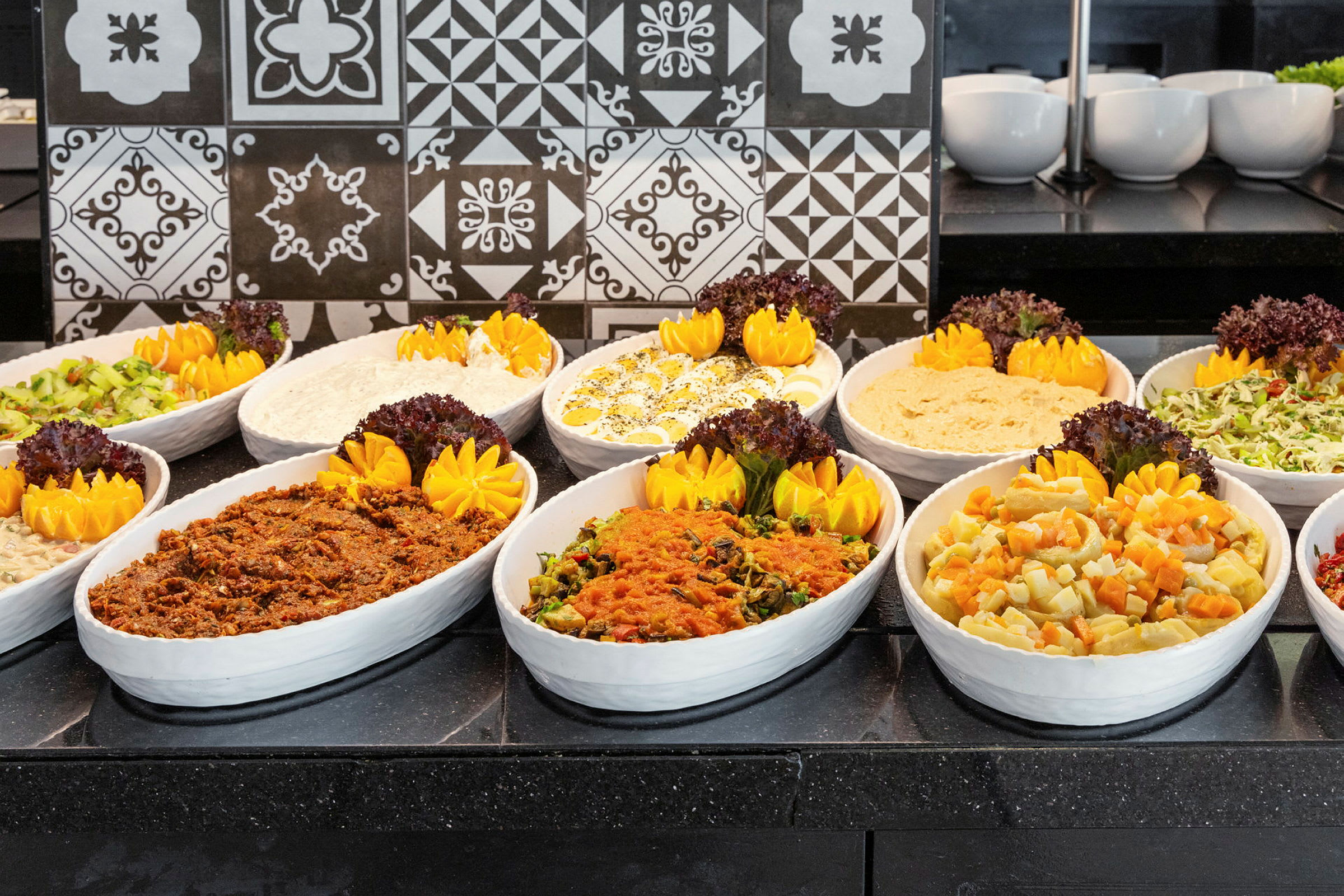 Forskellige retter præsenteret i hvide skåle på en buffet. (AI-genereret tekst)