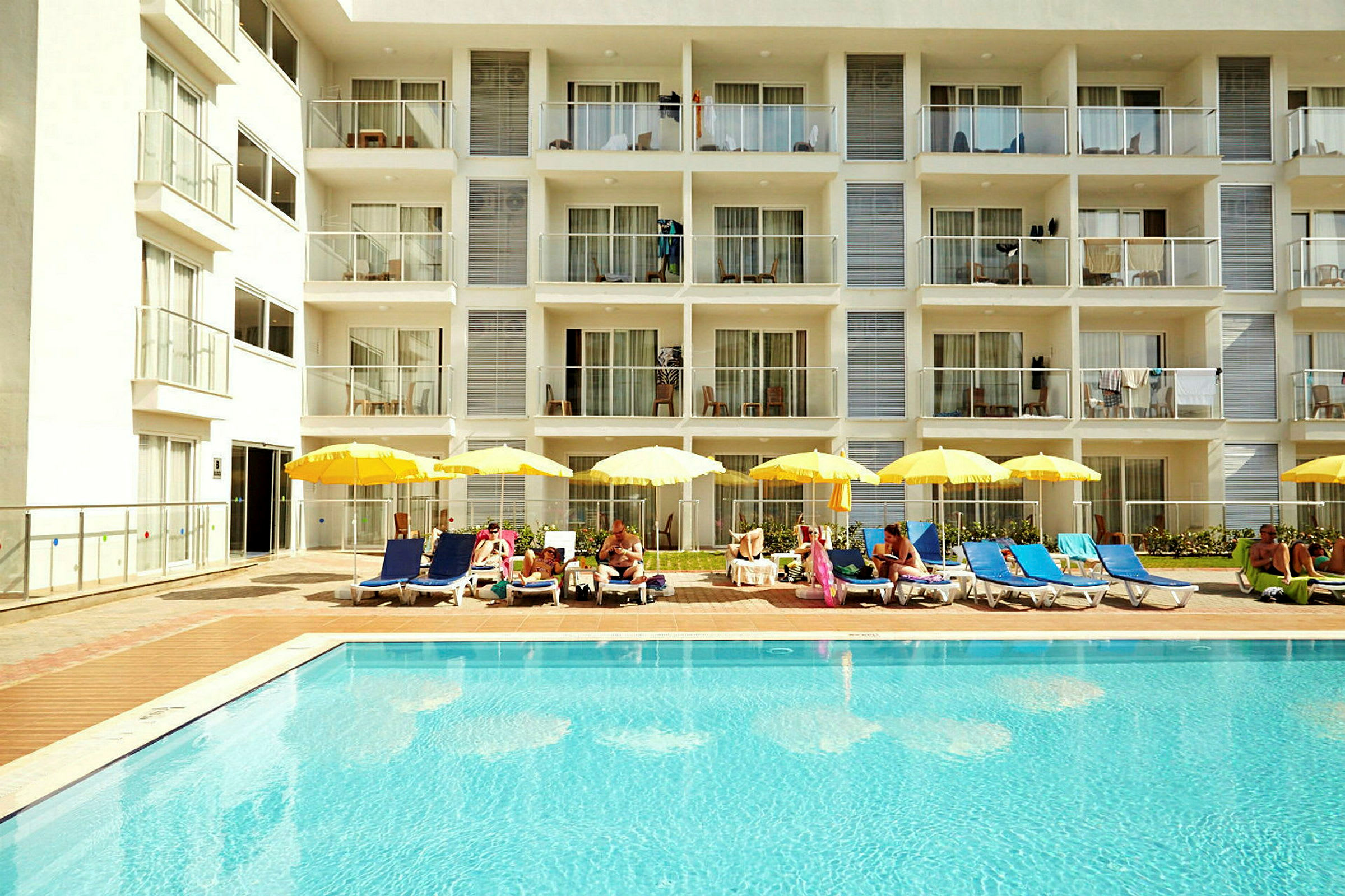 Udendørs swimmingpool med liggestole og parasoller foran et hotel. (AI-genereret tekst)