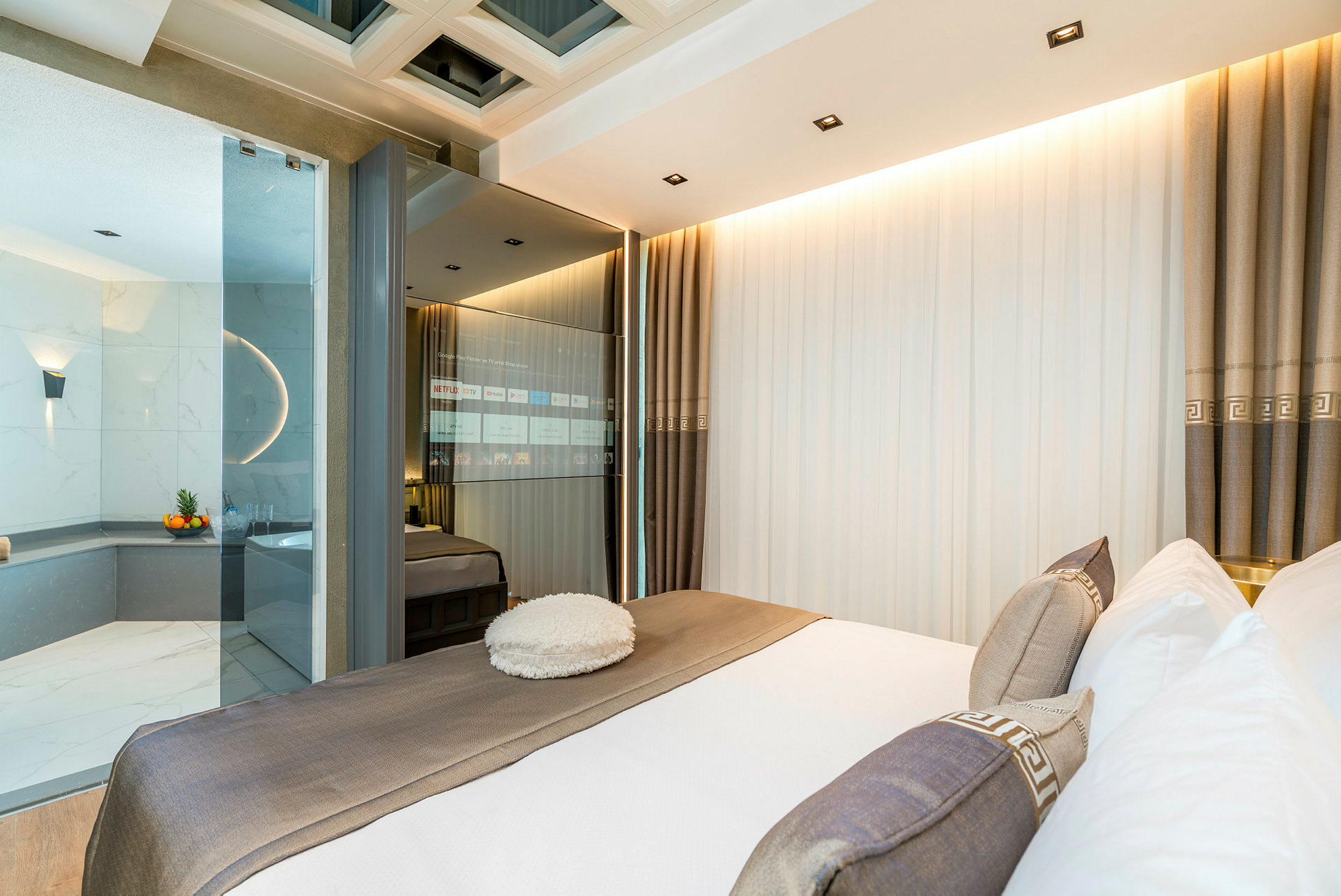 Moderne hotelværelse med en bred seng, glasvæg og udsigt til et marmorbeklædt badekar. (AI-genereret tekst)