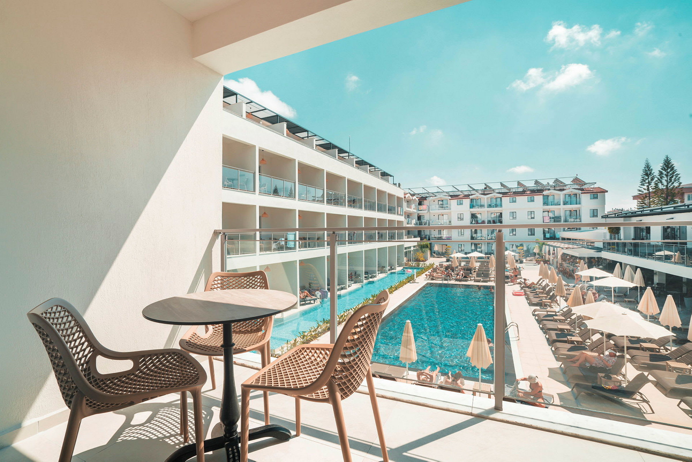 Udsigt fra en balkon mod en pool og hotelbygninger. (AI-genereret tekst)