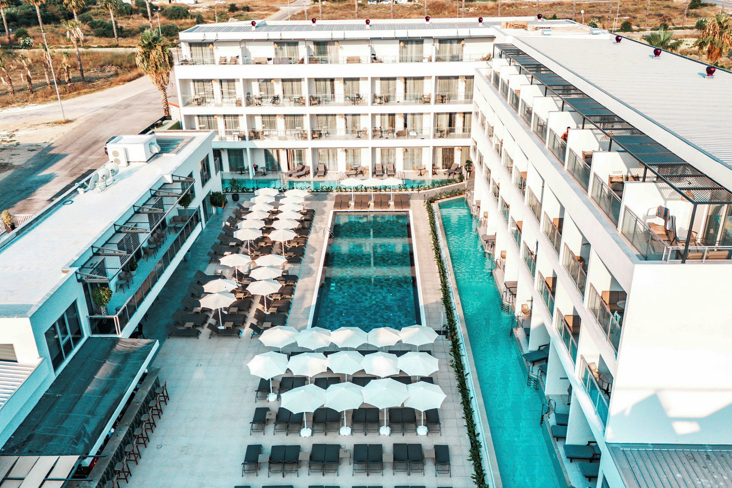 Hotelområde med bygninger omkring en pool, liggestole og parasoller. (AI-genereret tekst)