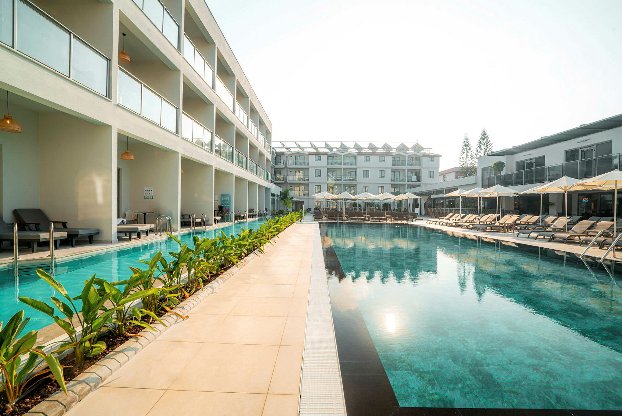 Udendørs pool ved hotelområde med liggestole og moderne bygninger. (AI-genereret tekst)
