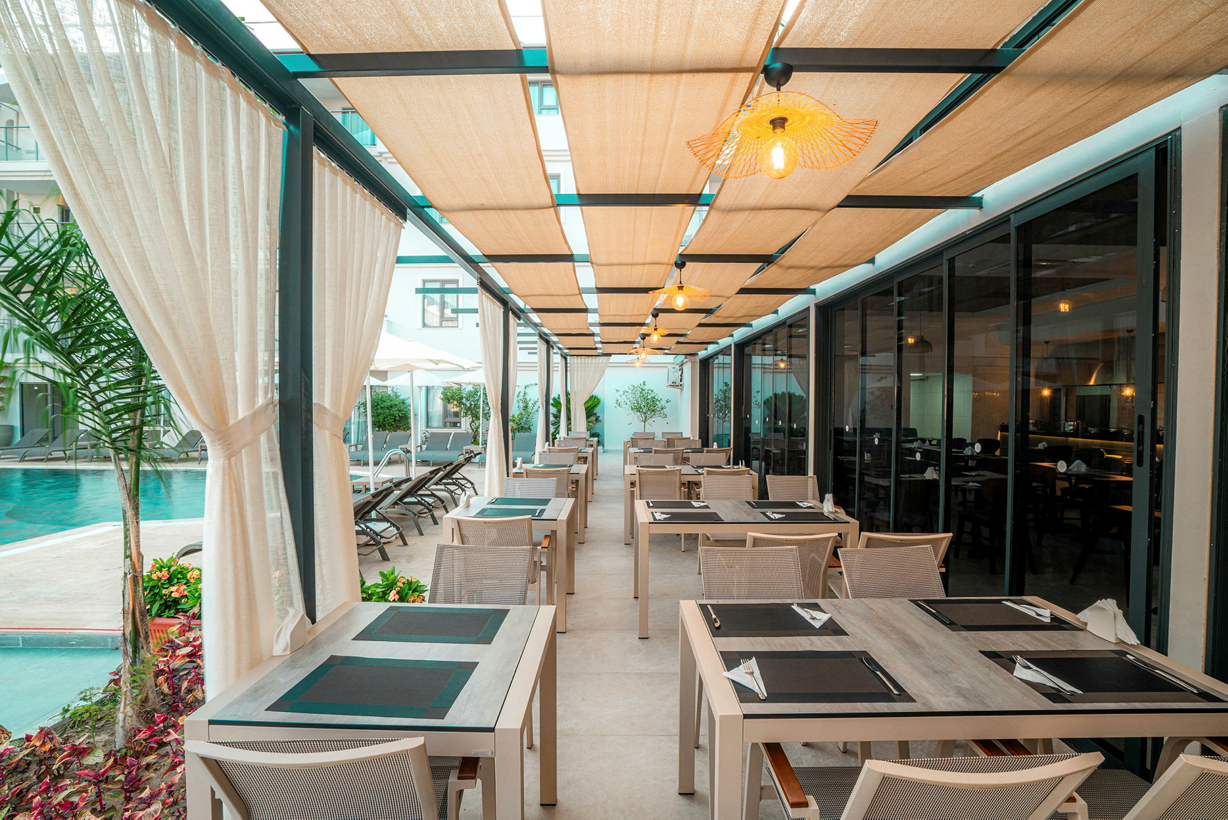Billede af en udendørs restaurant med borde og stole under et tag med lys, ved siden af en pool. (AI-genereret tekst)