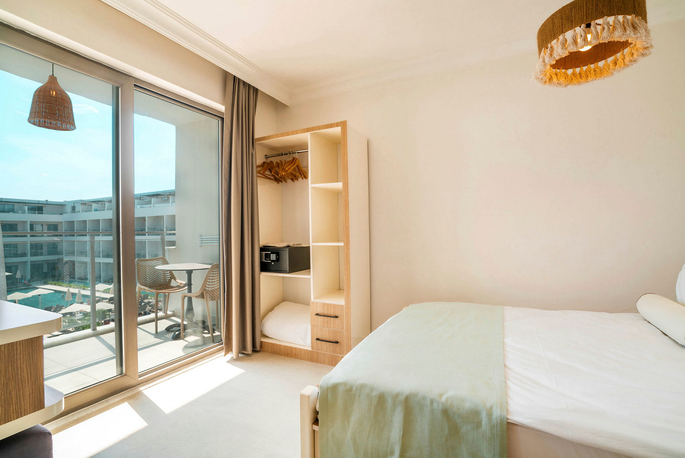 Hotelværelse med seng, garderobe og altan med udsigt til en pool. (AI-genereret tekst)