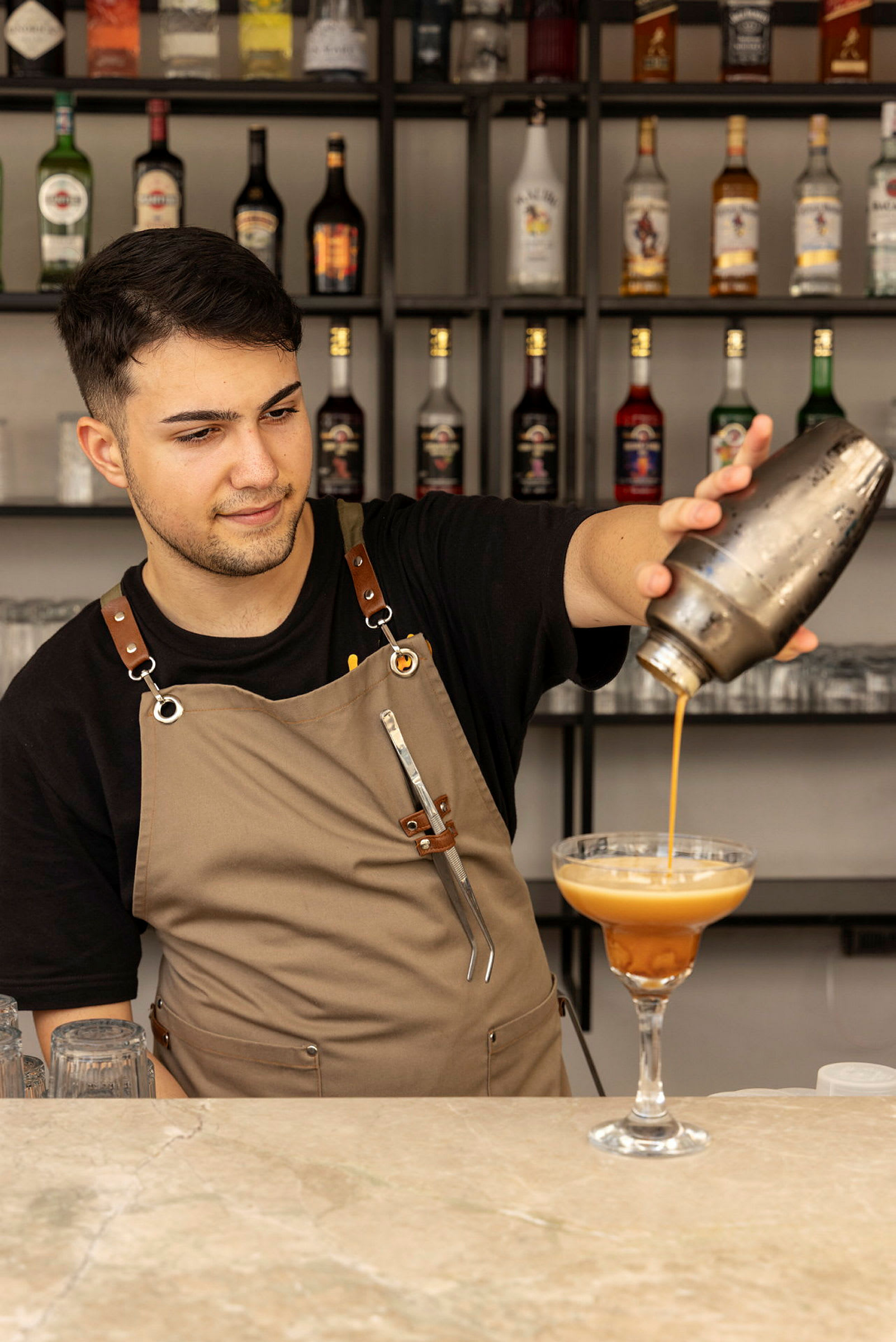 En bartender hælder en drink fra en shaker i et cocktailglas. (AI-genereret tekst)