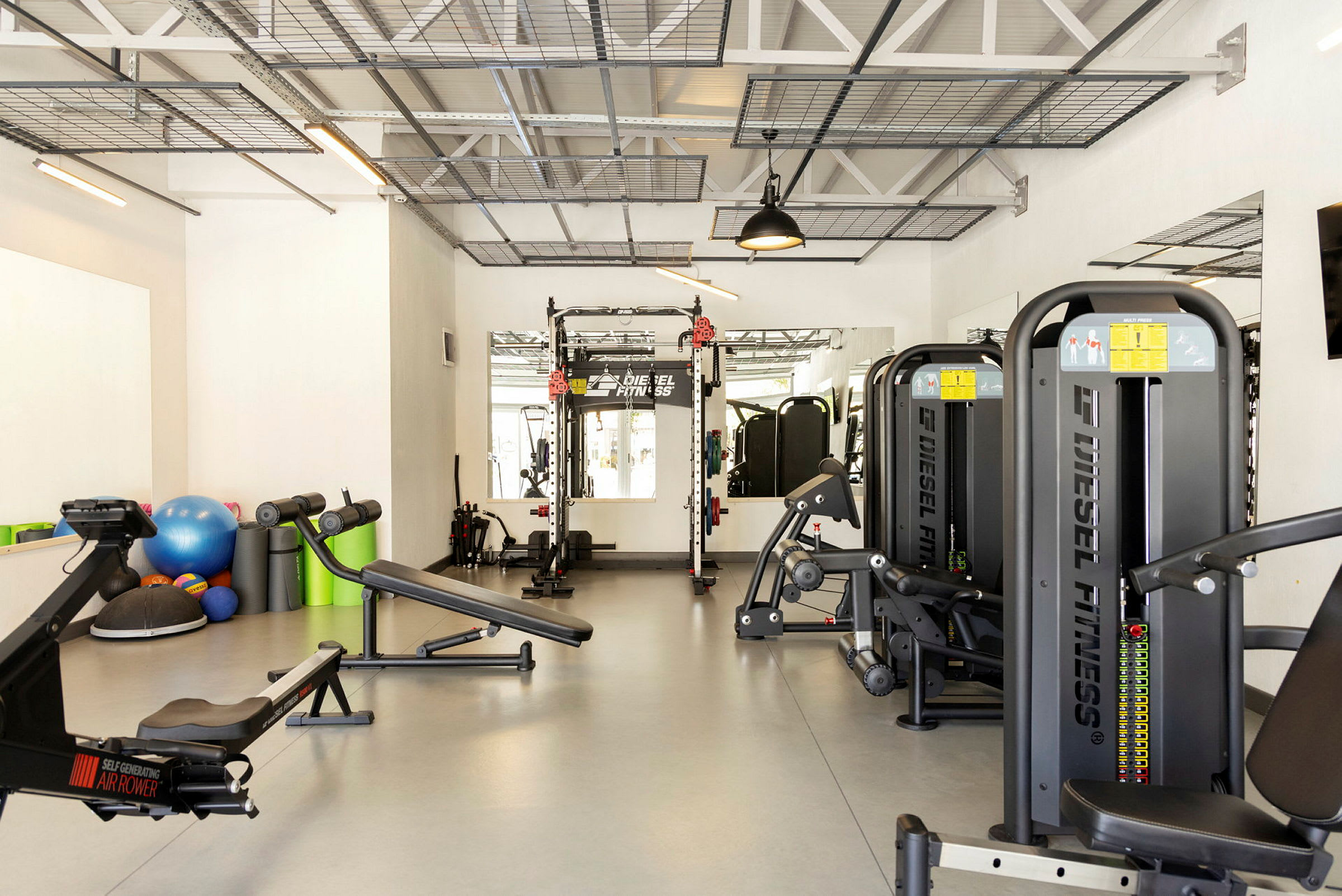 Et fitnesscenter med forskellige træningsmaskiner, træningsbænke og tilbehør som medicinbolde og fitnessbolde. (AI-genereret tekst)