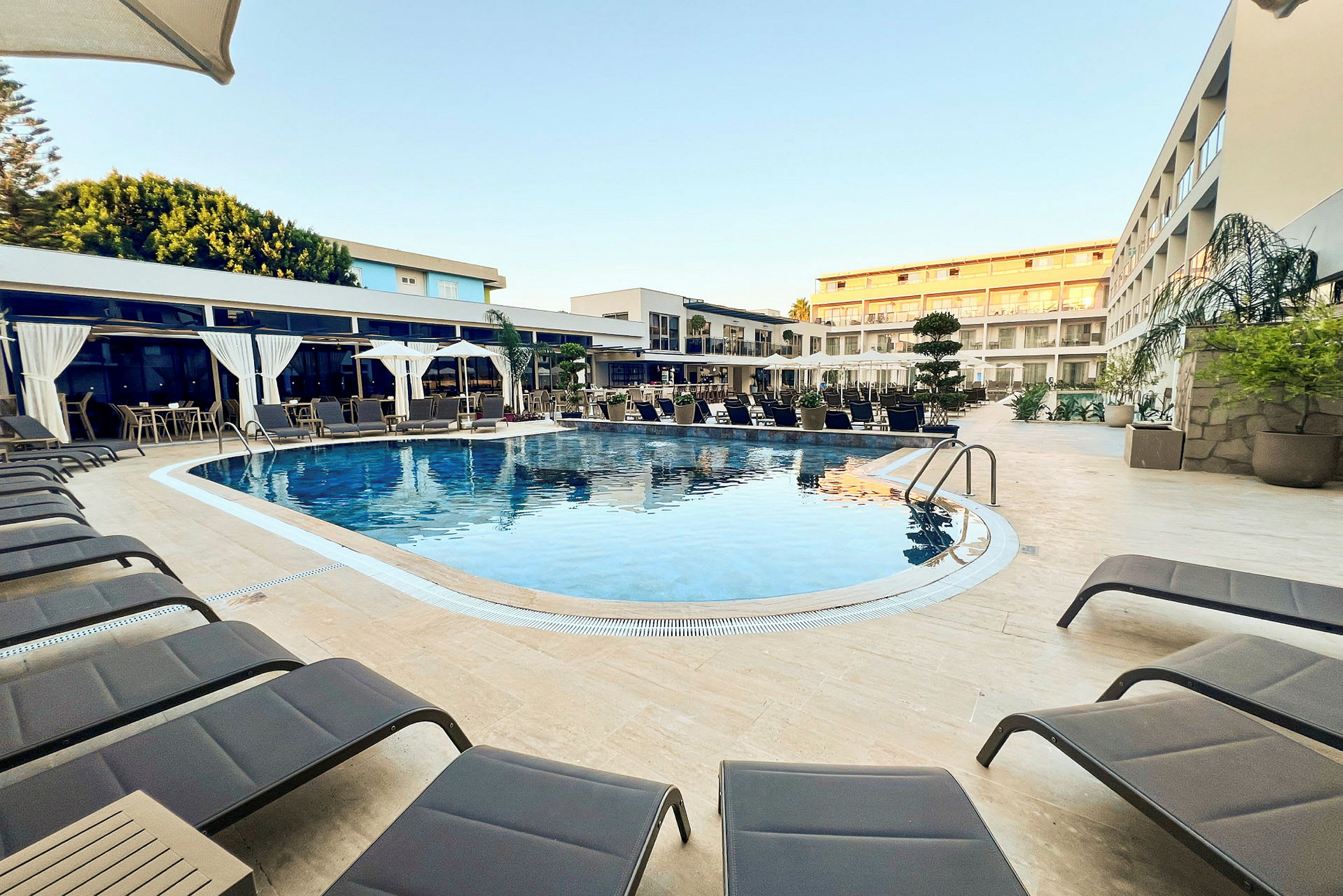 Udendørs pool med solstole og hotelbygninger i baggrunden. (AI-genereret tekst)