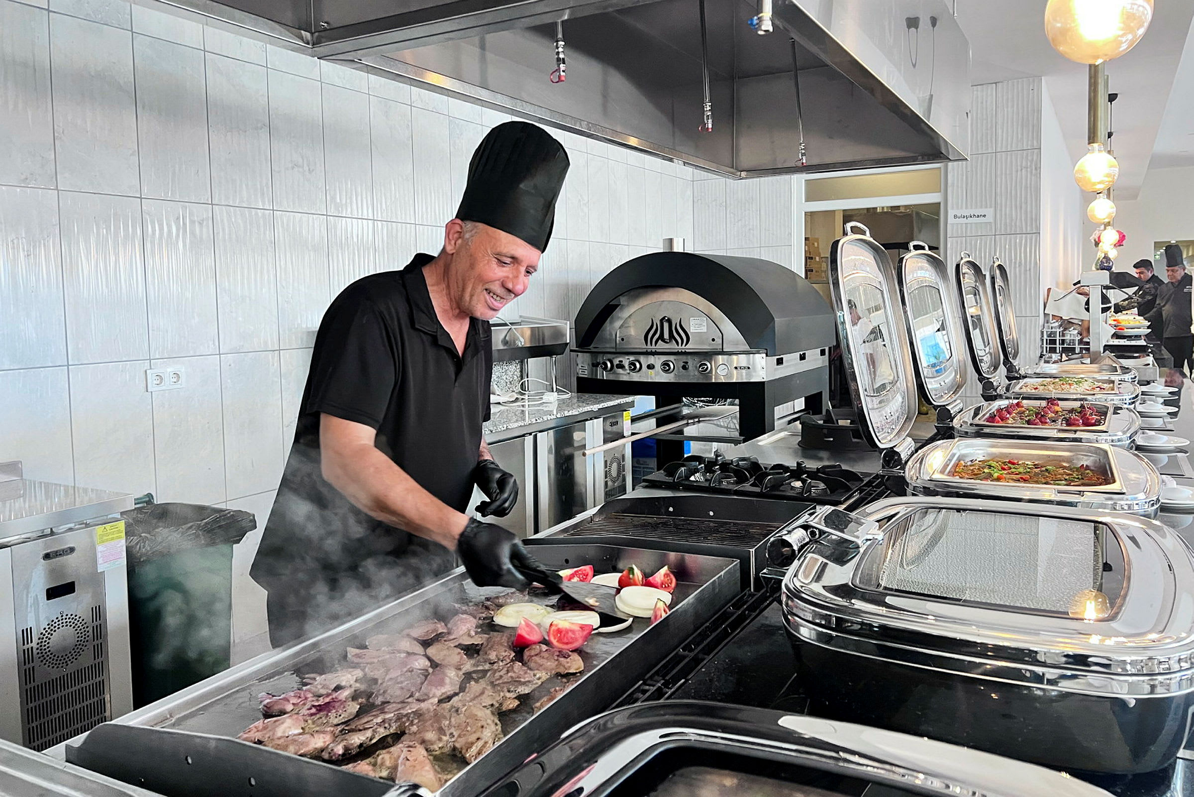 En kok laver mad på en grill i en buffémiljø. (AI-genereret tekst)