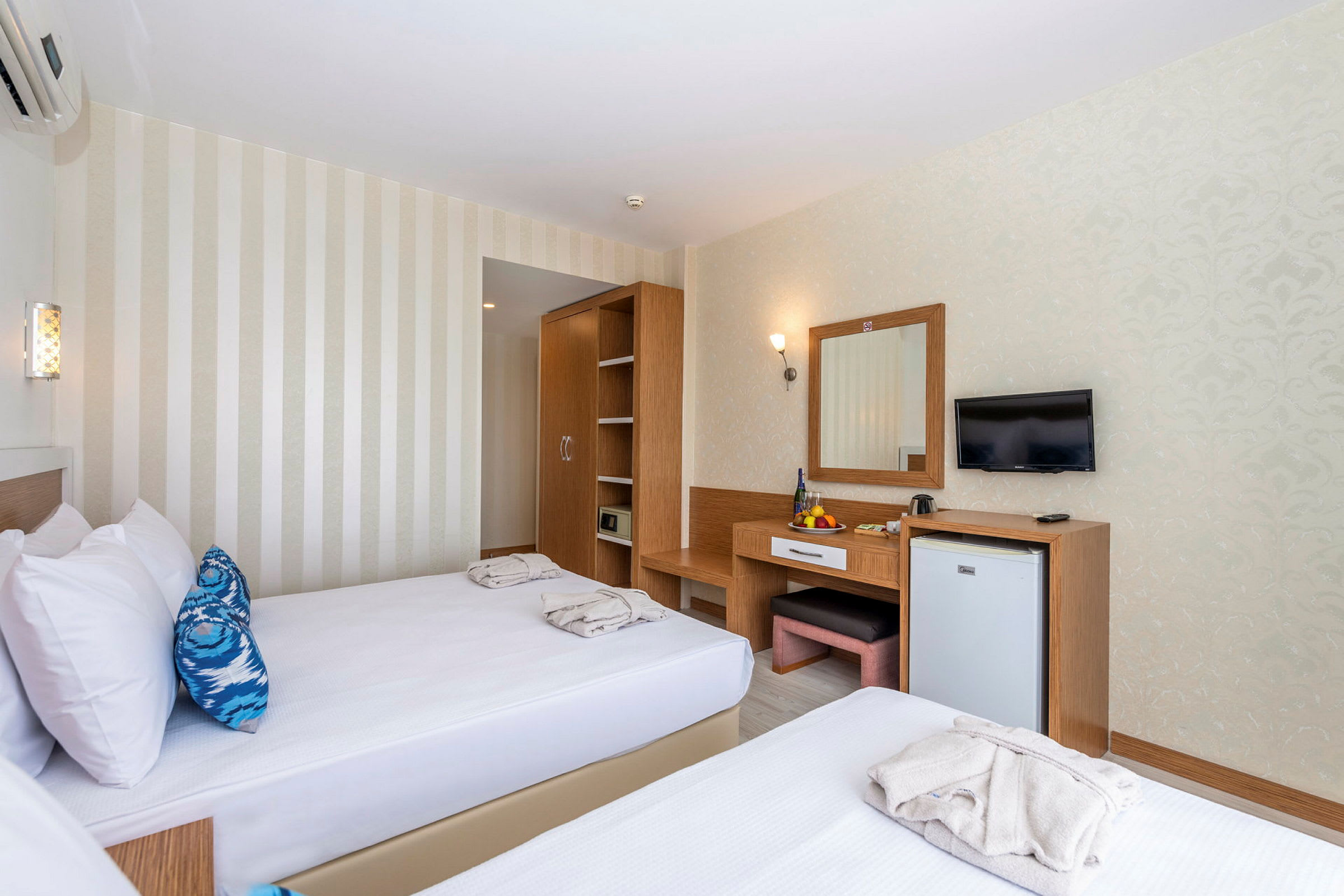 Hotelværelse med to enkeltsenge, et skab, et skrivebord med spejl og et vægmonteret TV. (AI-genereret tekst)