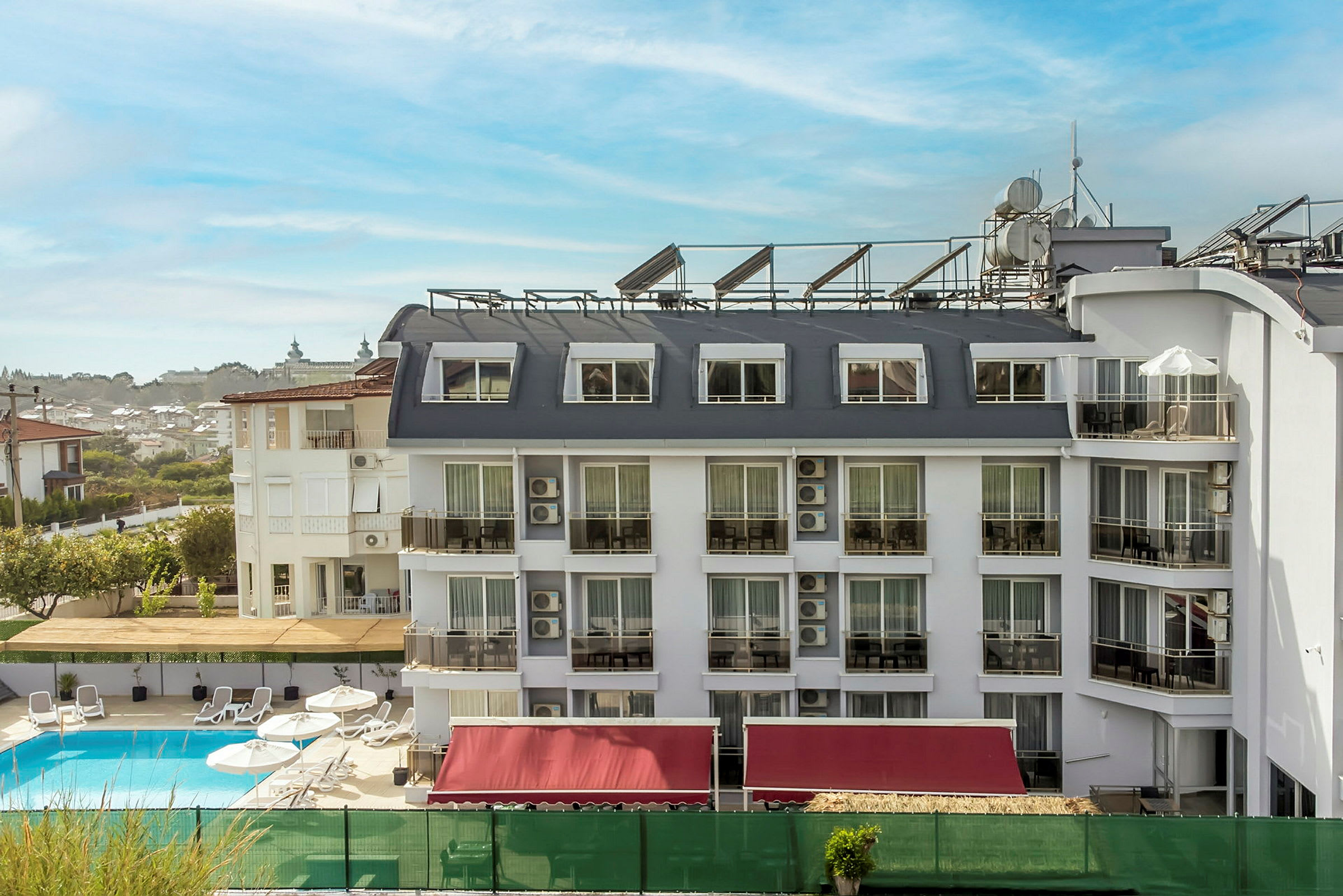 Et hotel med hvid facade og flere vinduer og altaner, en pool foran bygningen. (AI-genereret tekst)