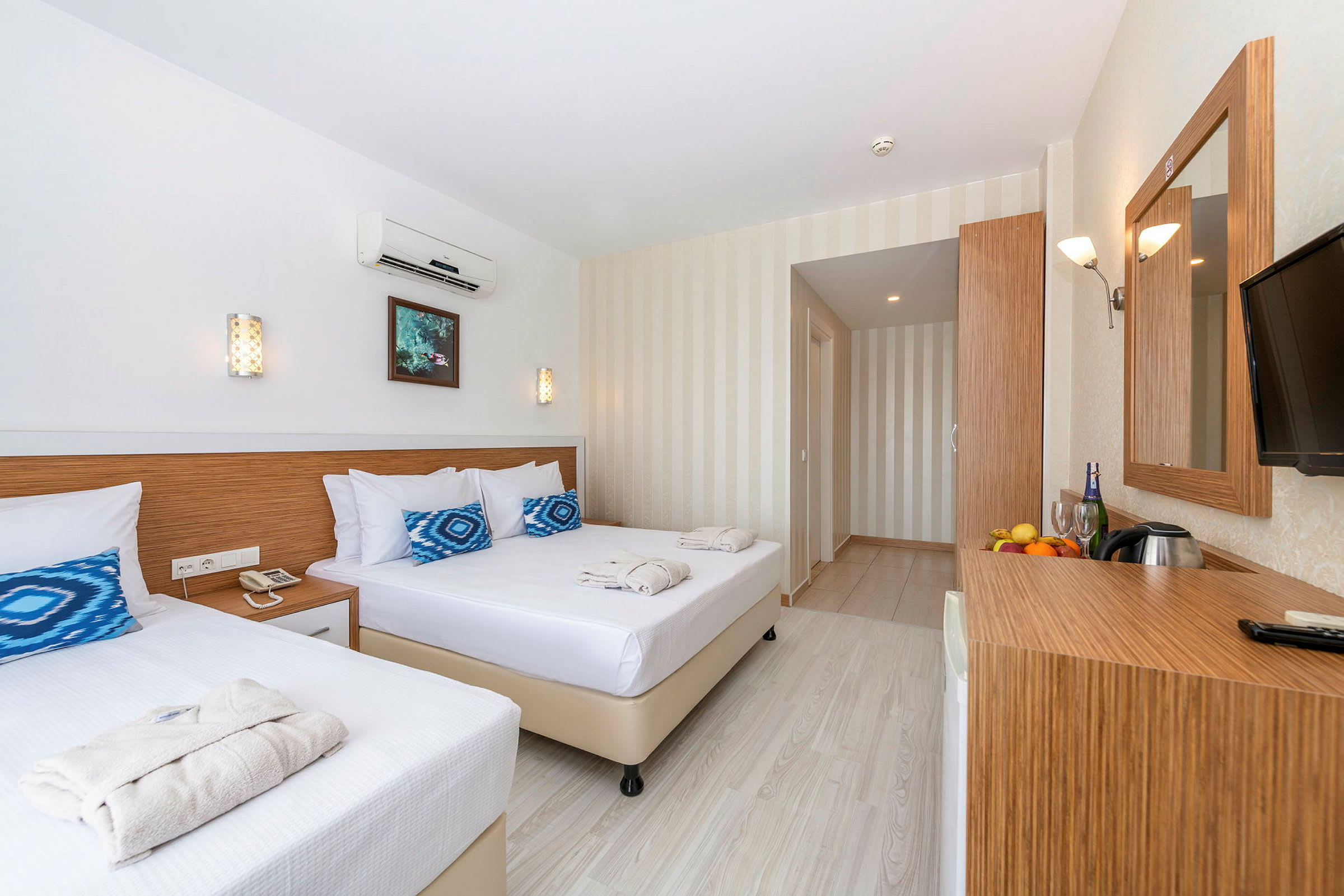 Et lyst og moderne hotelværelse med to senge, et spejl samt et skrivebord med frugt og drikke. (AI-genereret tekst)