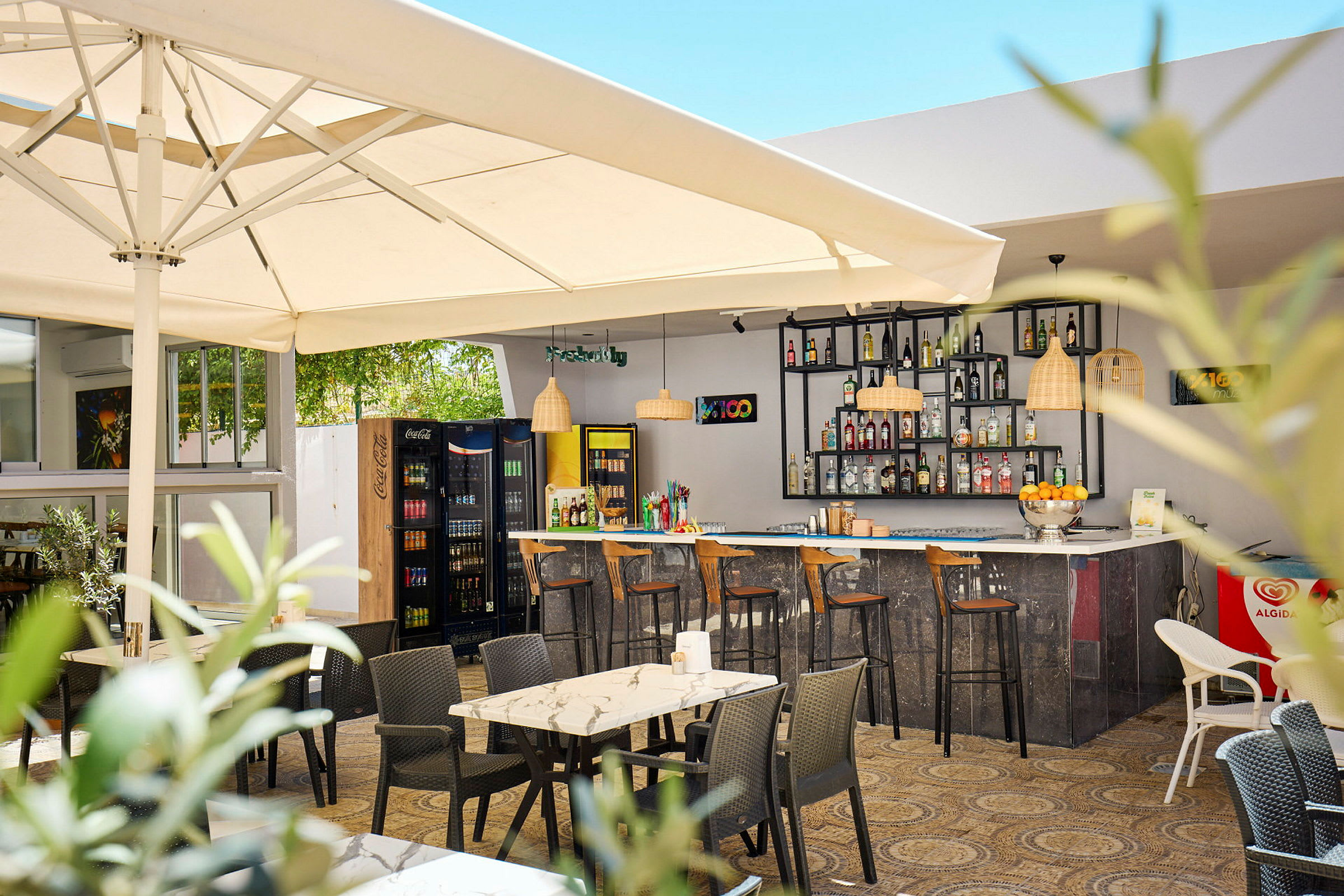 En udendørs bar med borde og stole under en parasol. (AI-genereret tekst)