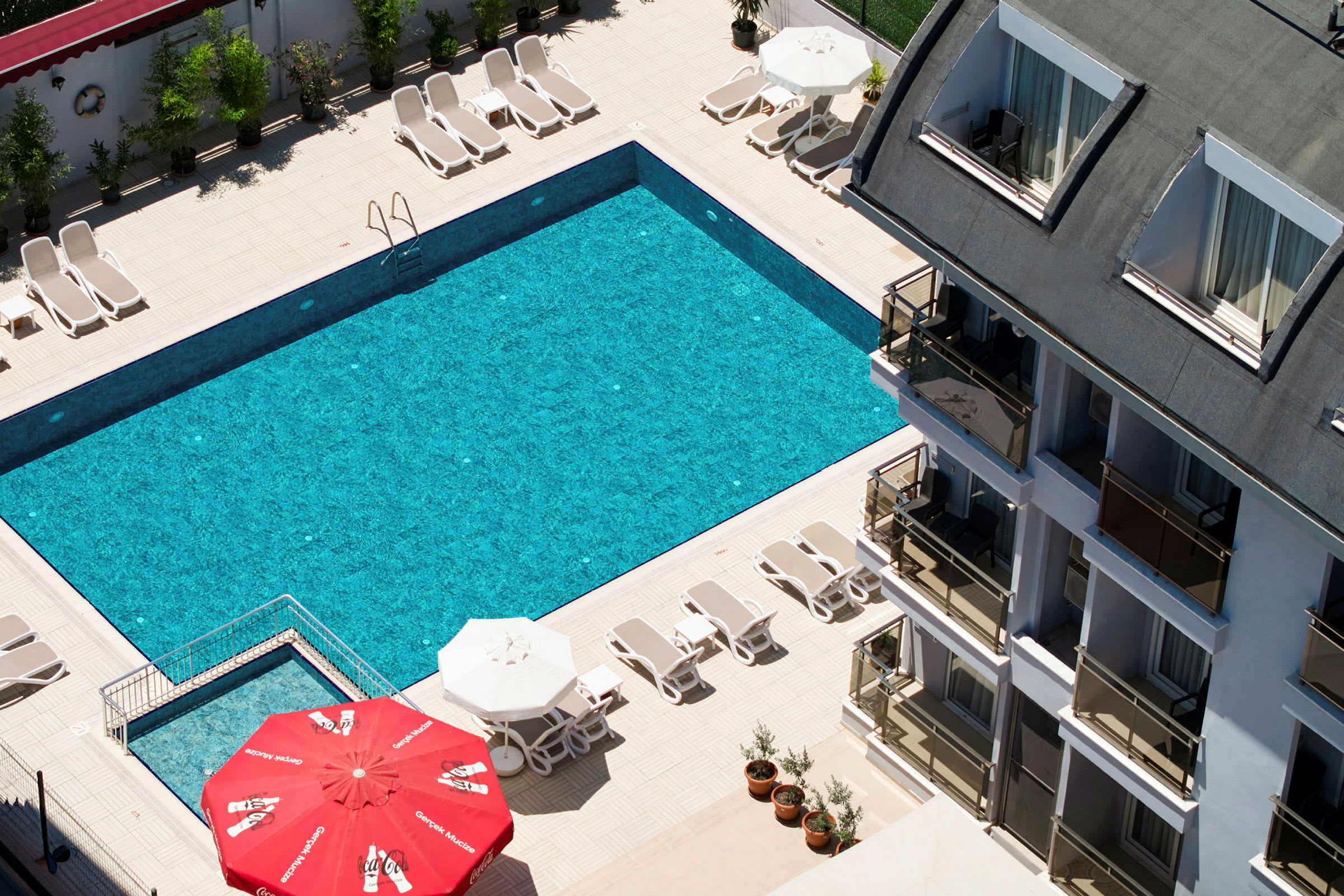 En hotelpool med solsenge og parasoller ved en flerfamiliebygning. (AI-genereret tekst)