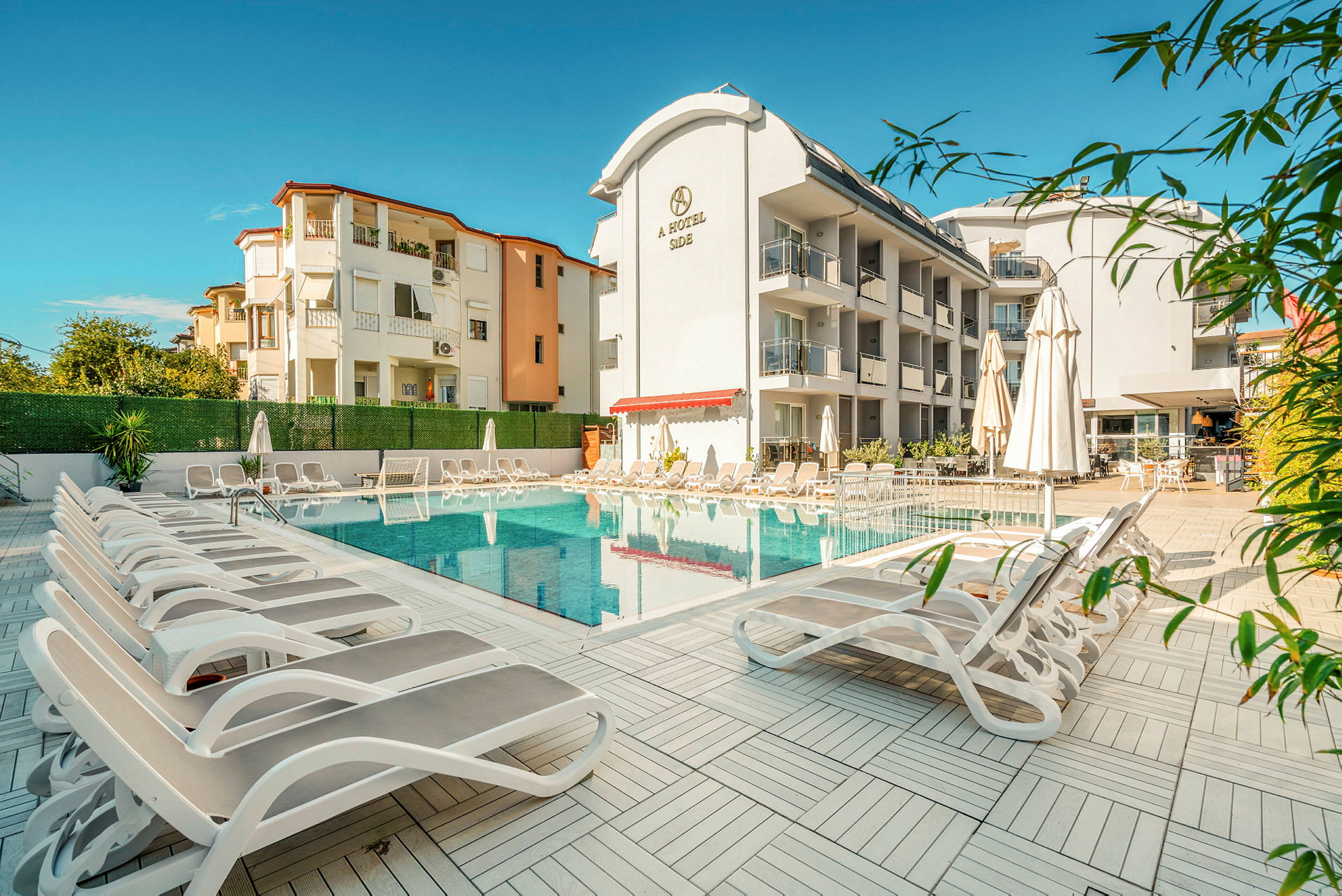 Billede af hotellets poolområde med liggestole og parasoller foran bygninger. (AI-genereret tekst)