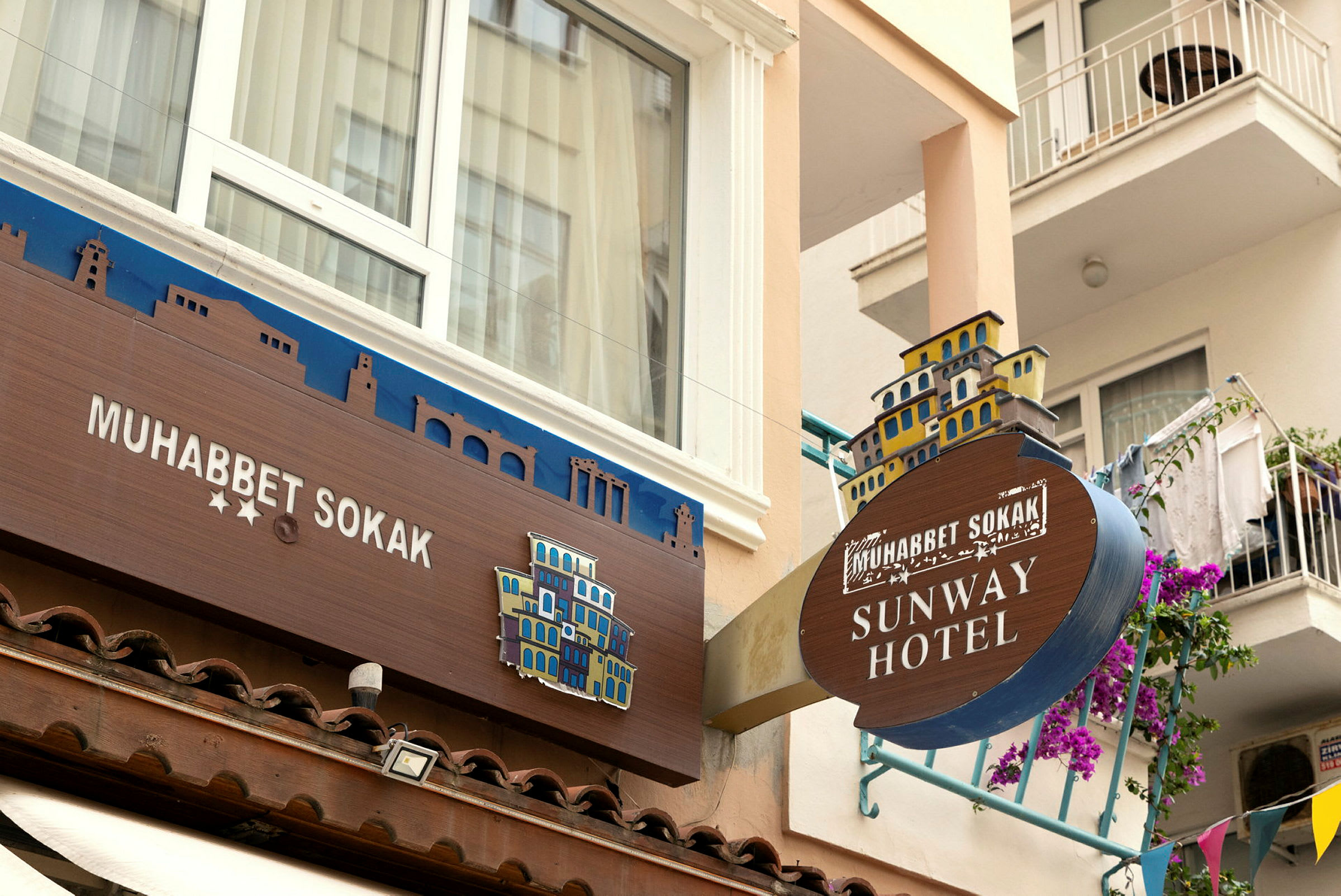 Billede af facade på et hotel med skilte, der viser navnene 'Muhabbet Sokak' og 'Sunway Hotel'. (AI-genereret tekst)