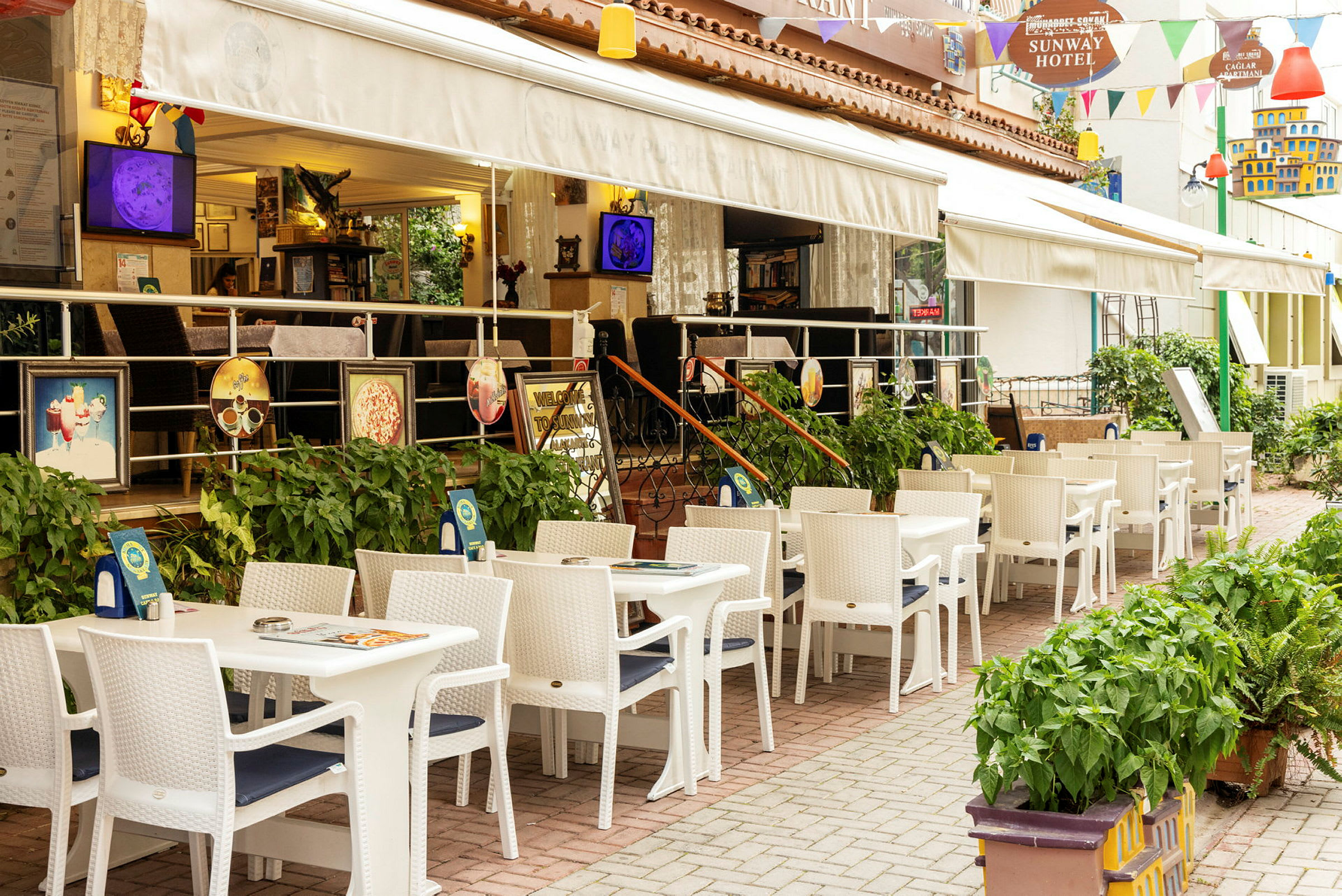 Restaurant med udendørs servering med hvide borde og stole ved et hotel. (AI-genereret tekst)