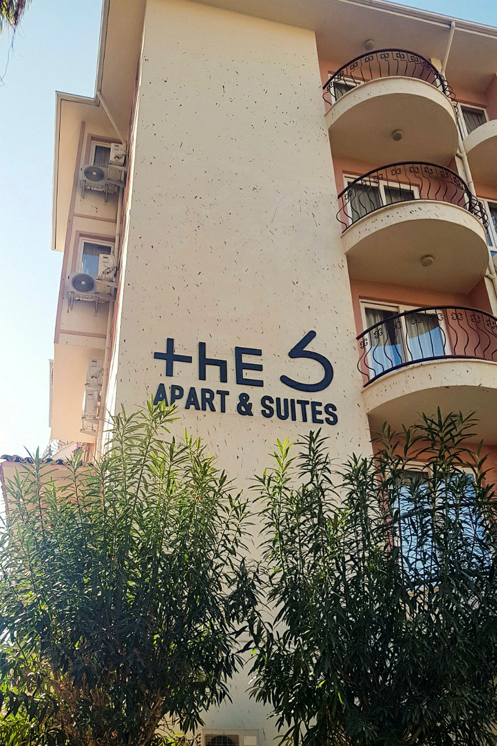 Bygning med et skilt, hvor der står "The S Apart & Suites", omgivet af træer. (AI-genereret tekst)