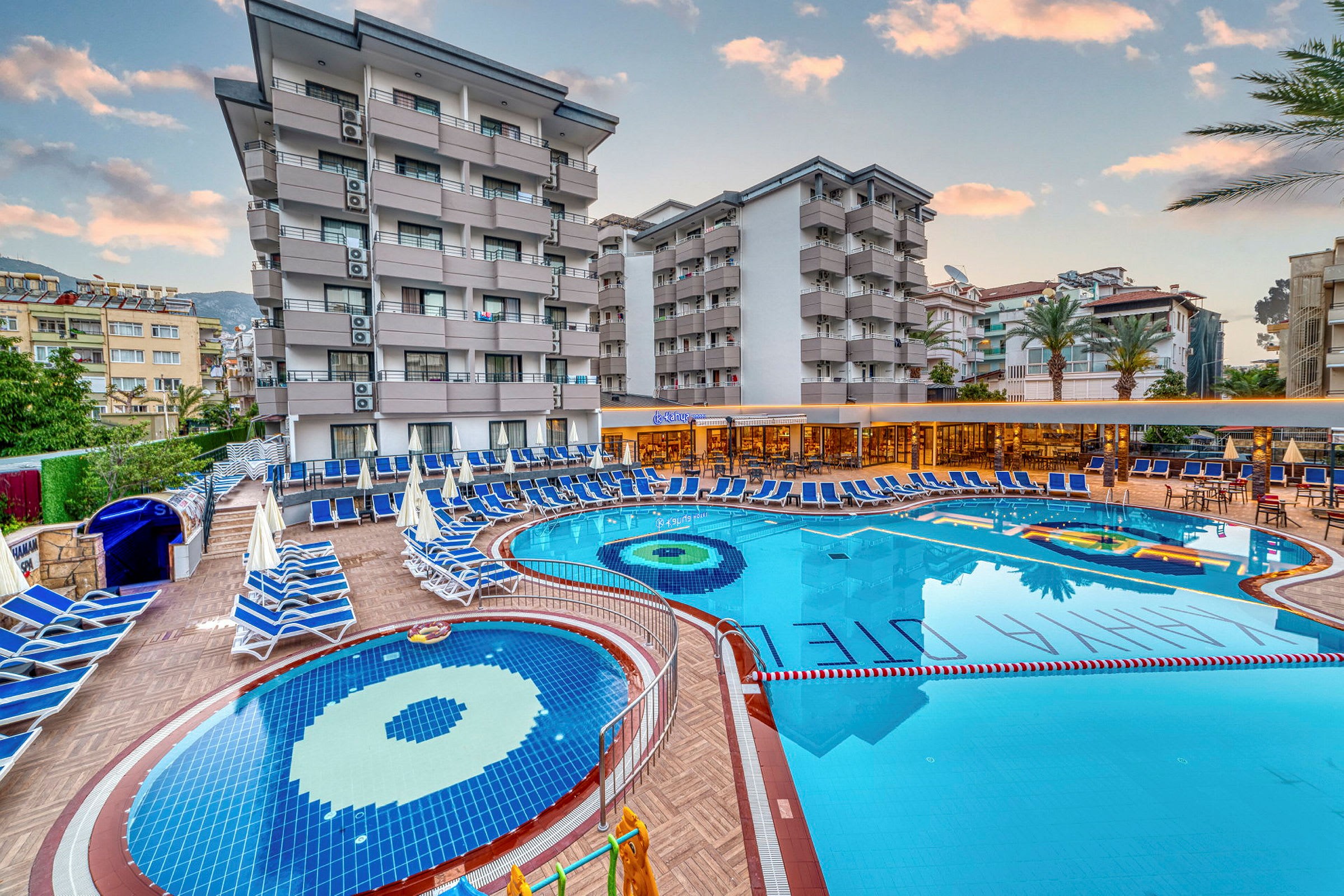 Hotelområde med pools, liggestole og bygninger i baggrunden. (AI-genereret tekst)