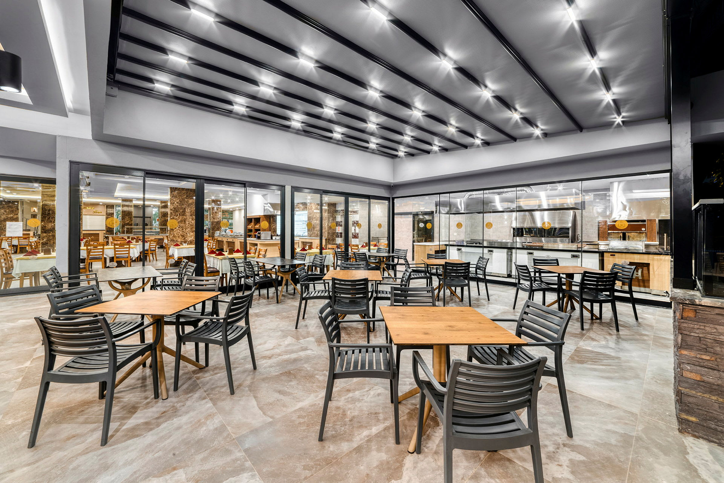 Et moderne restaurantområde med borde og stole foran et køkkenområde med glasvæg. (AI-genereret tekst)
