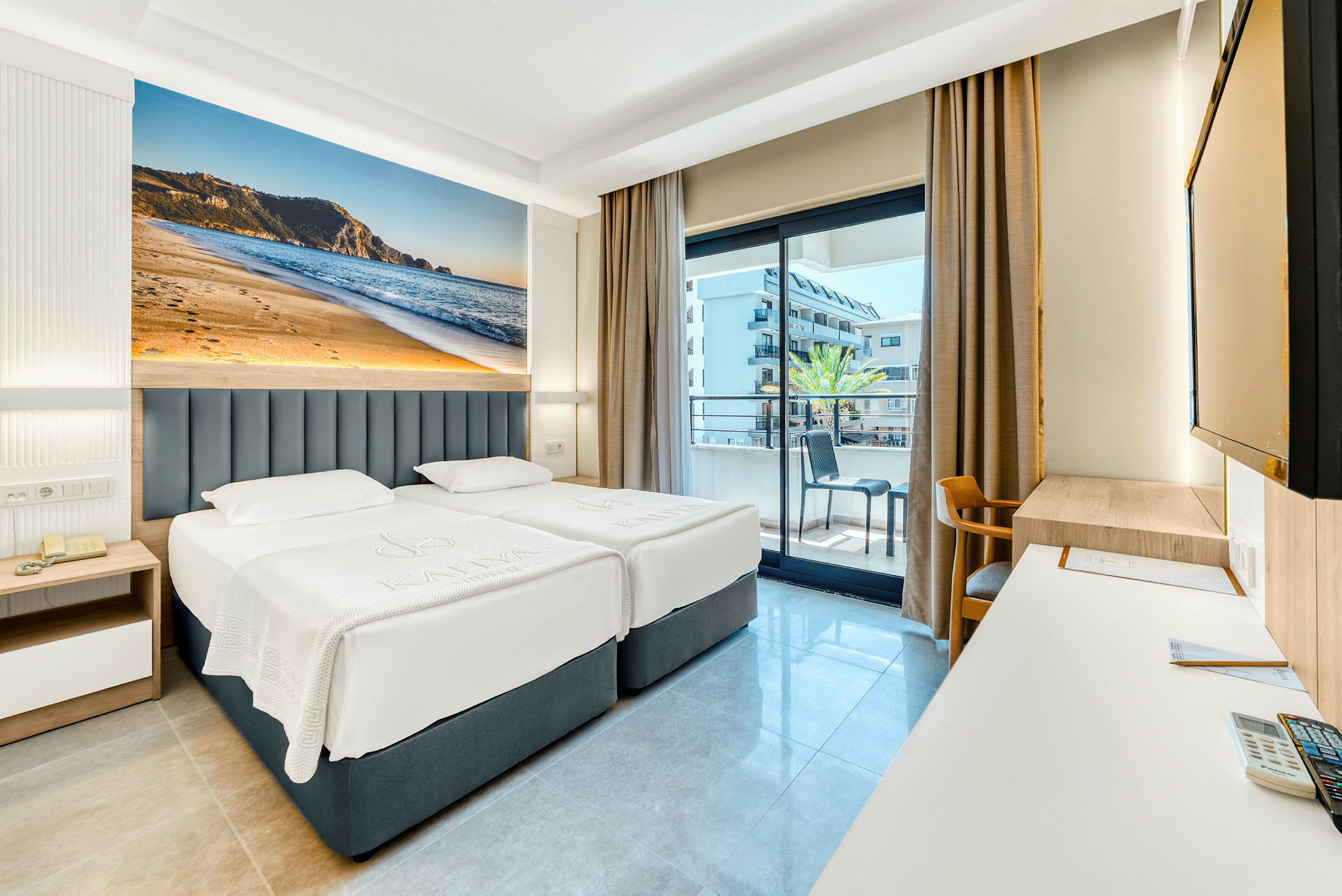 Hotelværelse med to enkeltsenge, balkon i baggrunden og stort fotografi af en strand på væggen. (AI-genereret tekst)