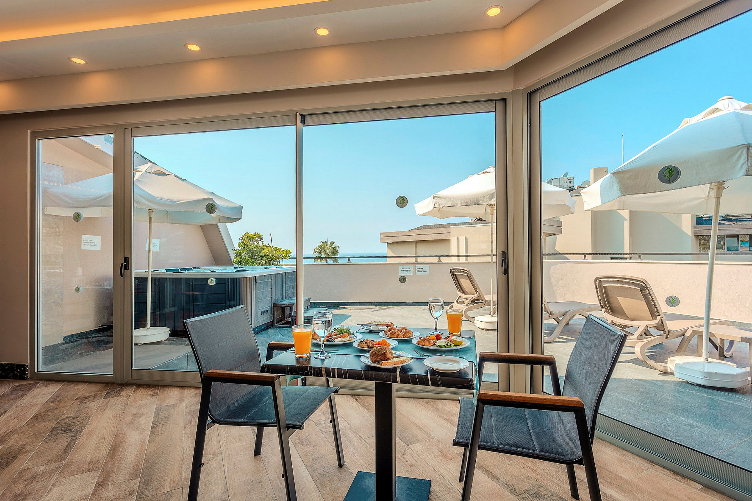 Udsigt fra et værelse med morgenmad på et bord og en terrasse med liggestole og parasoller. (AI-genereret tekst)