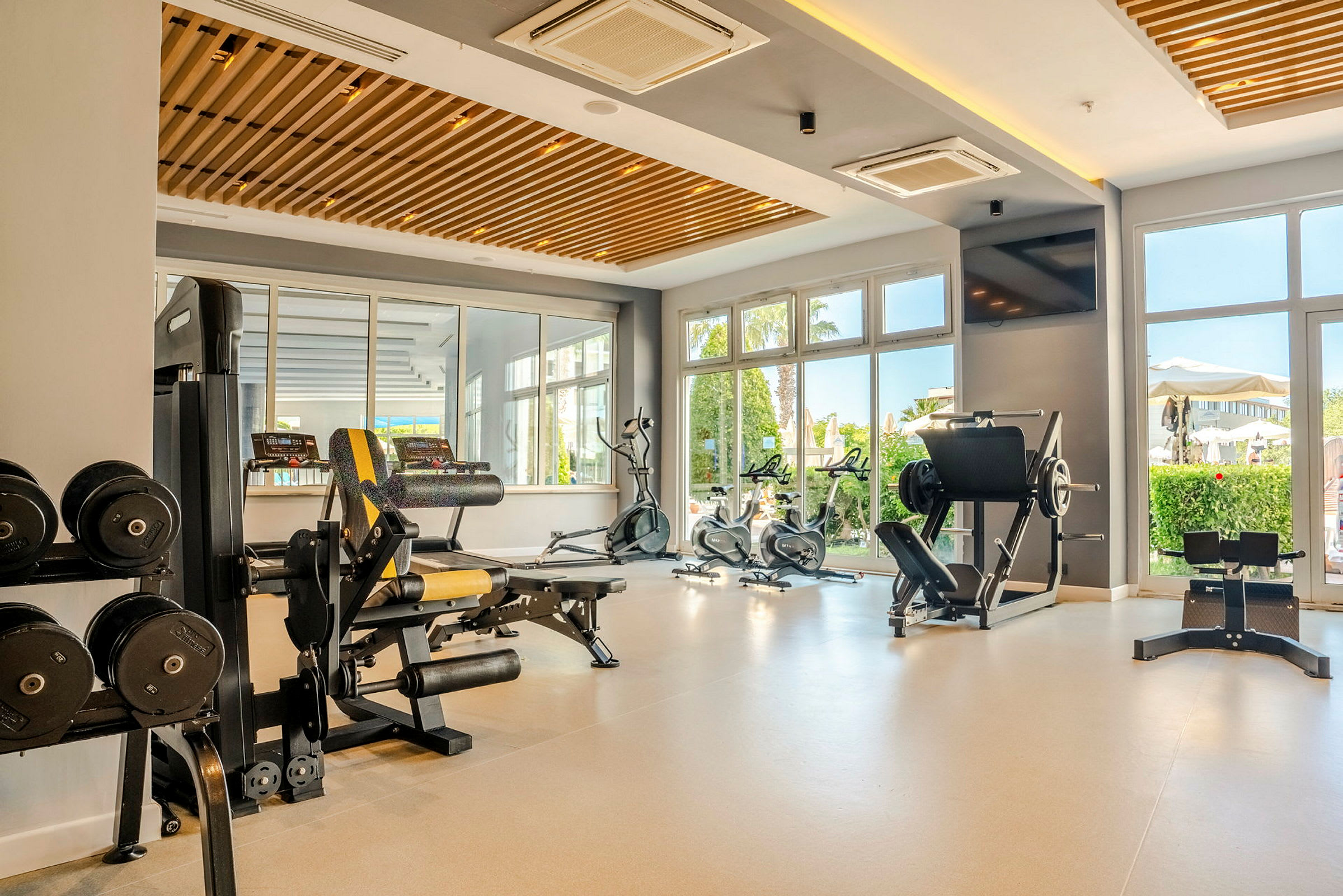Et fitnesscenter med forskellige træningsmaskiner, håndvægte og store vinduer, der lukker naturligt lys ind. (AI-genereret tekst)