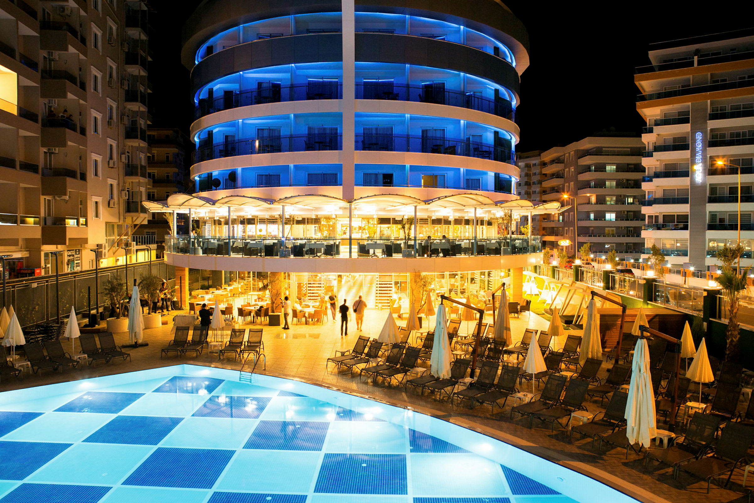 Et hotel med oplyst facade og poolområde om natten. (AI-genereret tekst)