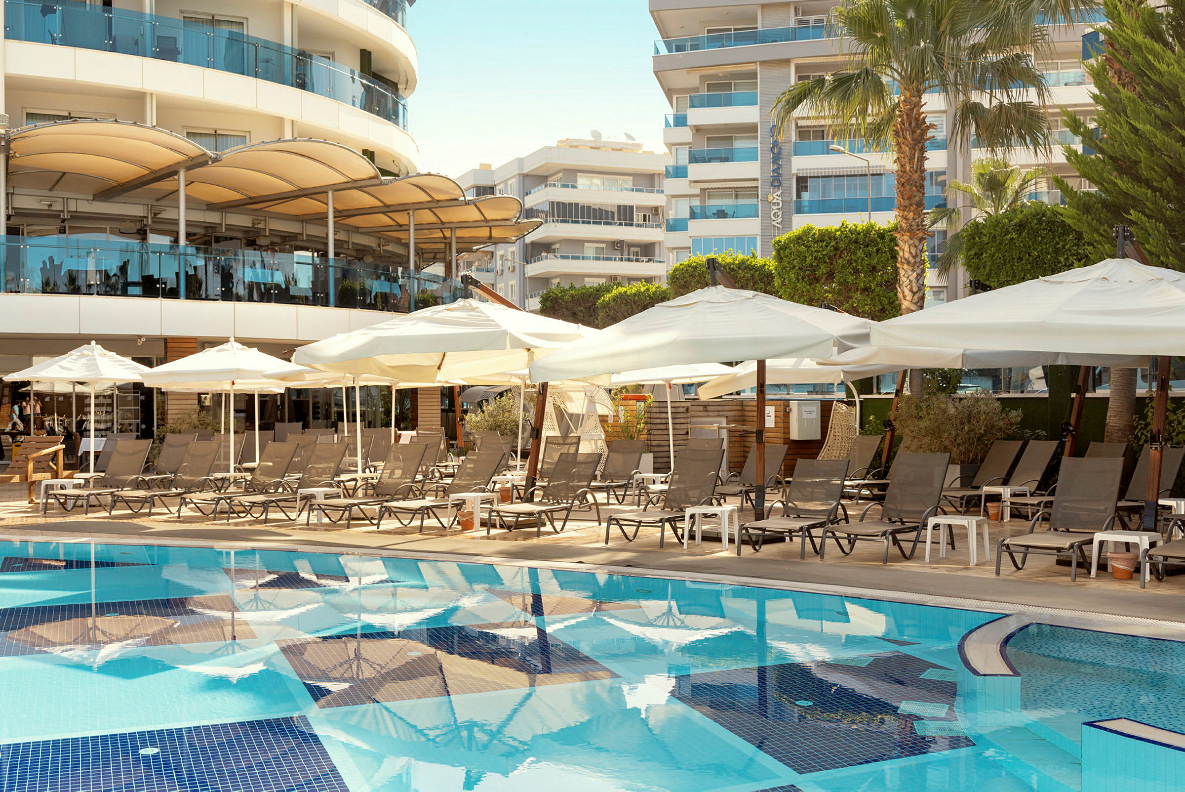 Poolområde med liggestole og parasoller foran hotelbygninger. (AI-genereret tekst)