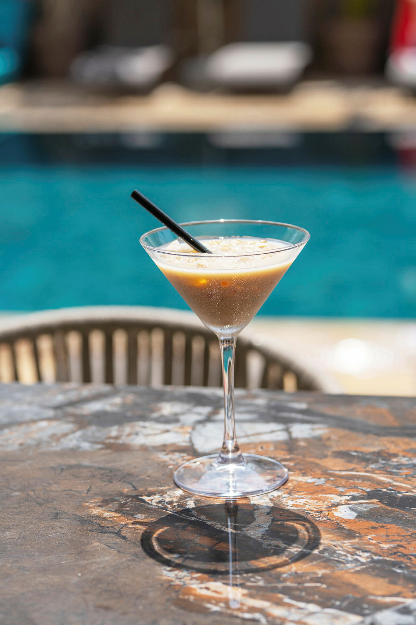 Et glas med en kold drink står på et bord nær en pool. (AI-genereret tekst)