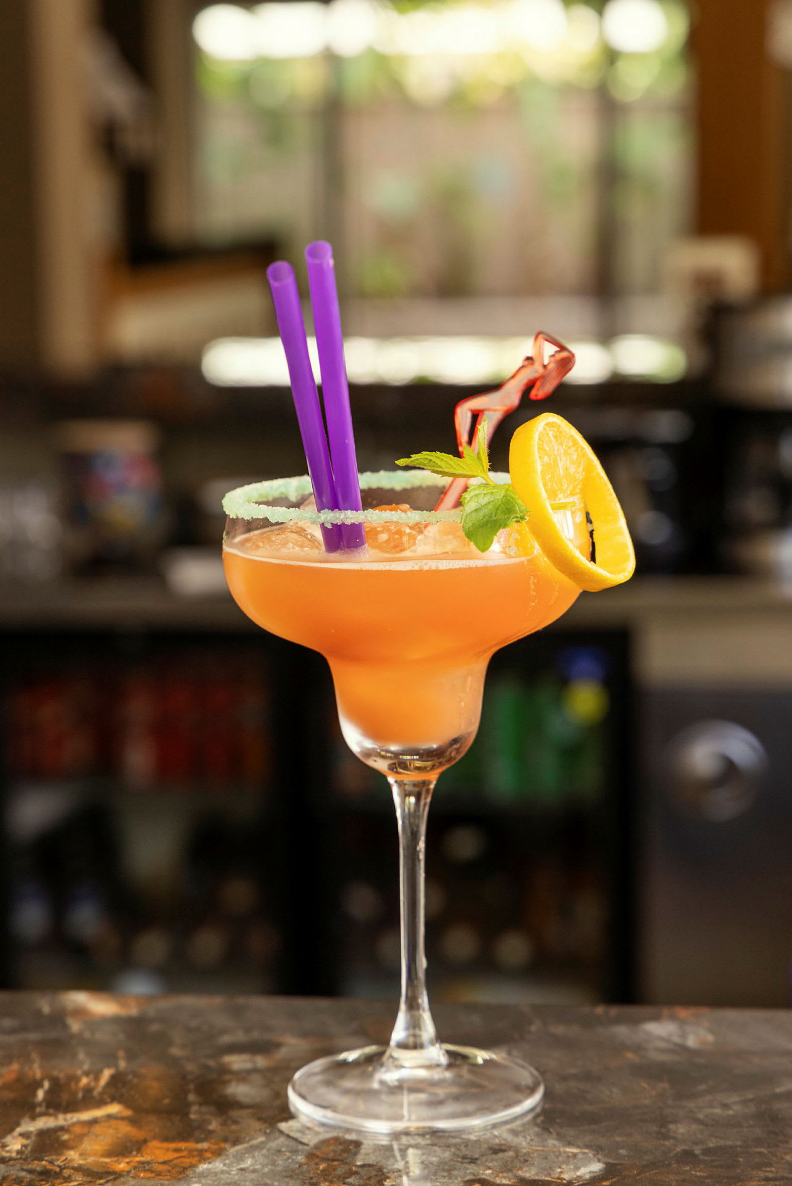En cocktail serveret i et glas med en citronskive, mynteblade og sugerør. (AI-genereret tekst)