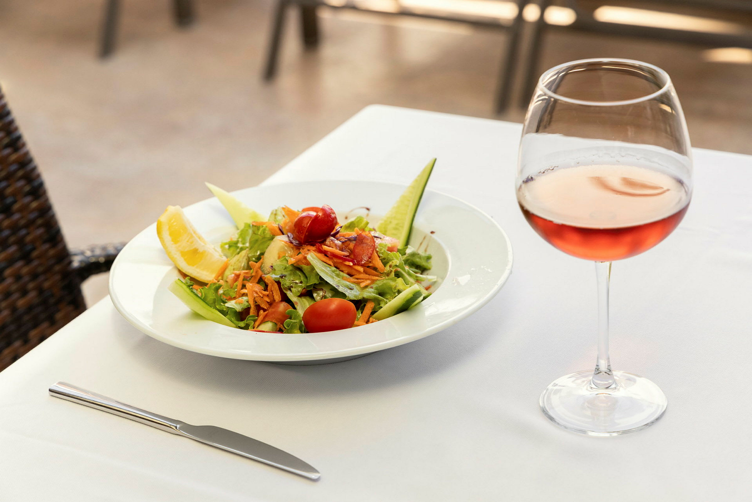 En tallerken med salat og et glas rosévin på et dækket bord. (AI-genereret tekst)