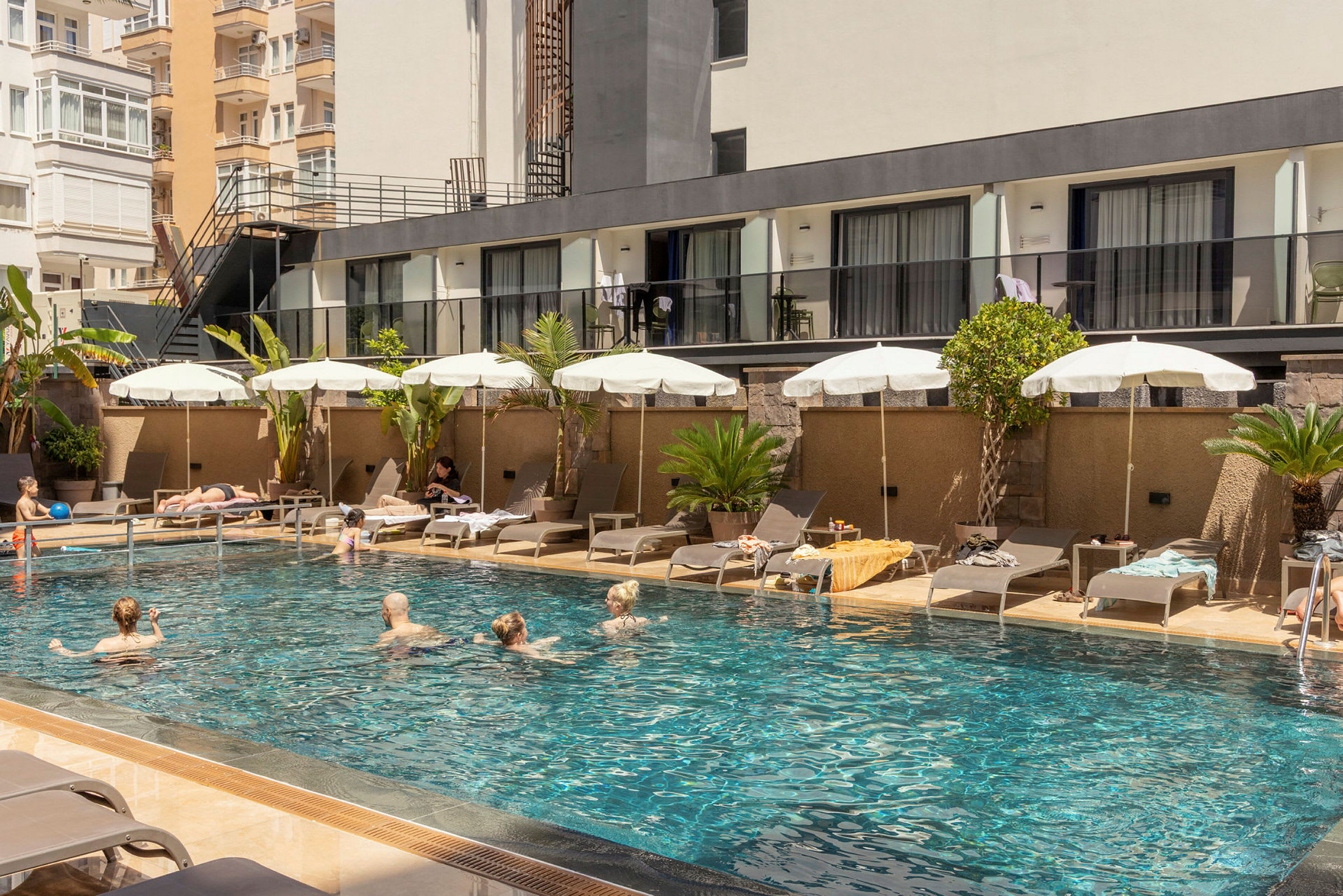 Udendørs poolområde ved et hotel med liggestole og parasoller, omgivet af bygninger. (AI-genereret tekst)