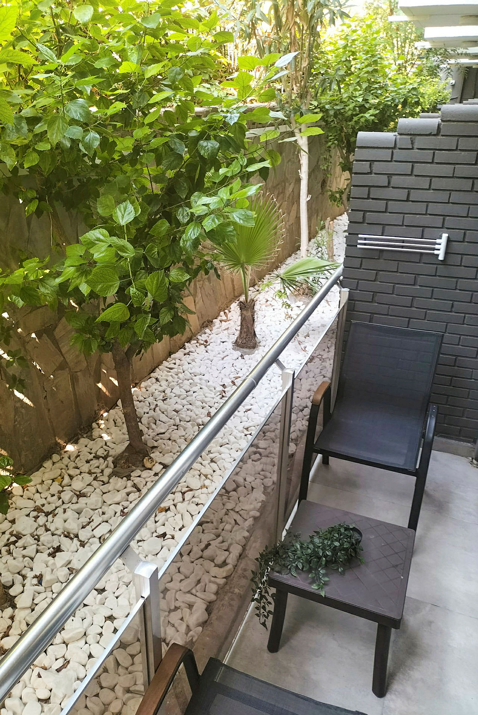 En lille udendørs plads med to stole og et bord, med grønne planter og stenbelægning langs siden. (AI-genereret tekst)