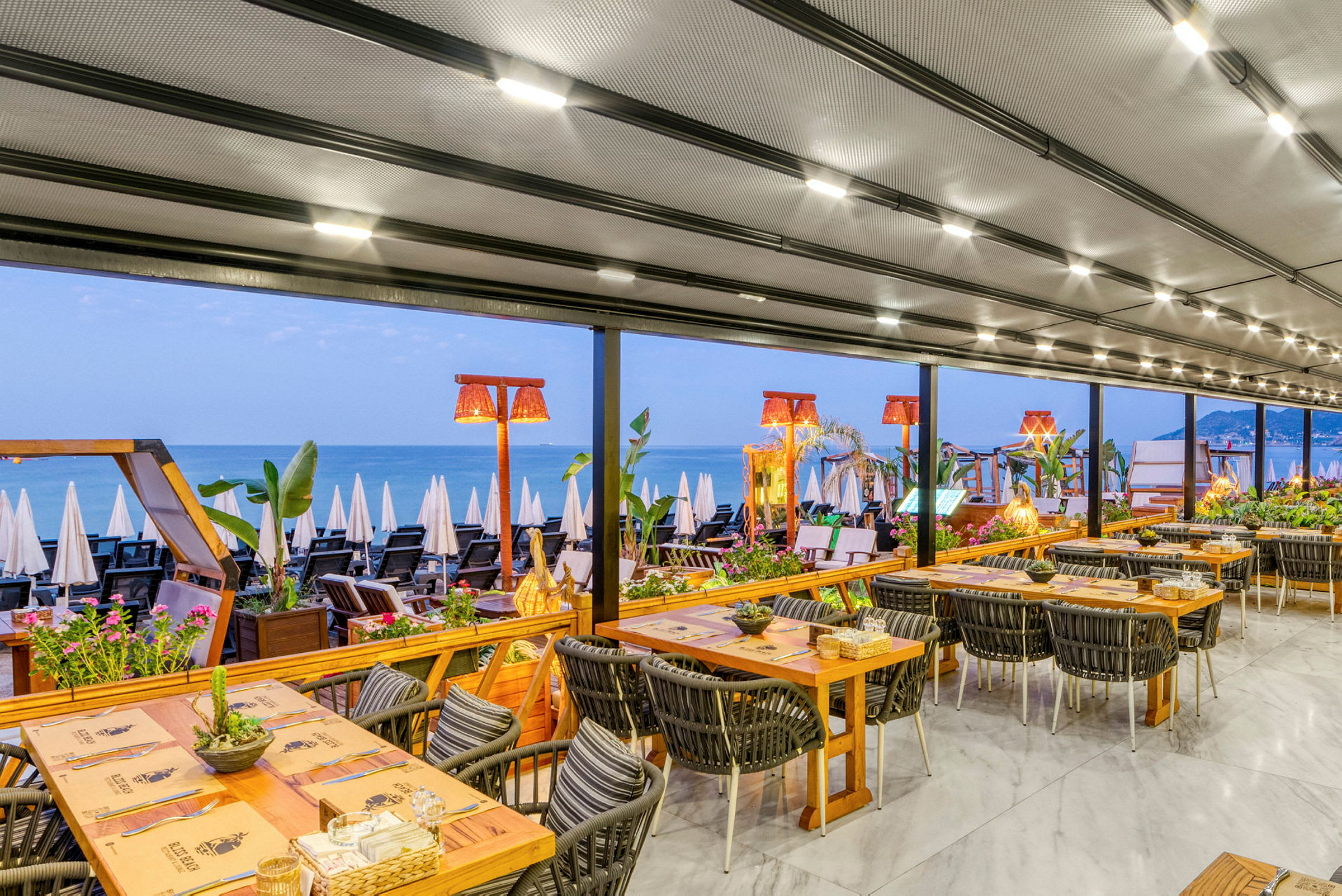 En restaurant med udsigt over en strand og havet, bordene er dækket til måltid. (AI-genereret tekst)