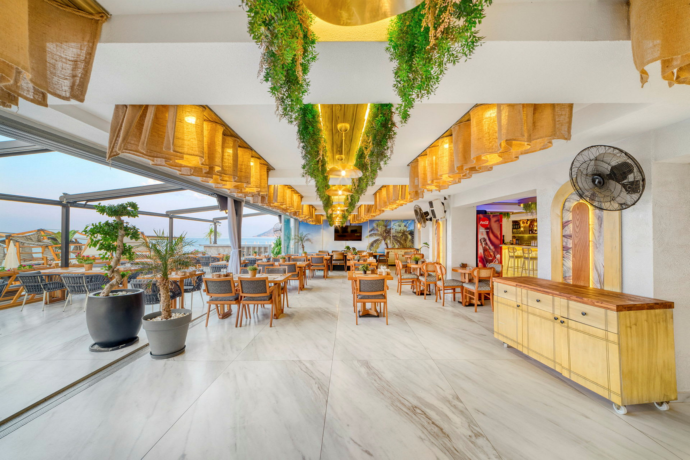 Restaurantindretning med borde og stole, grønne dekorationer og lyse lamper. (AI-genereret tekst)