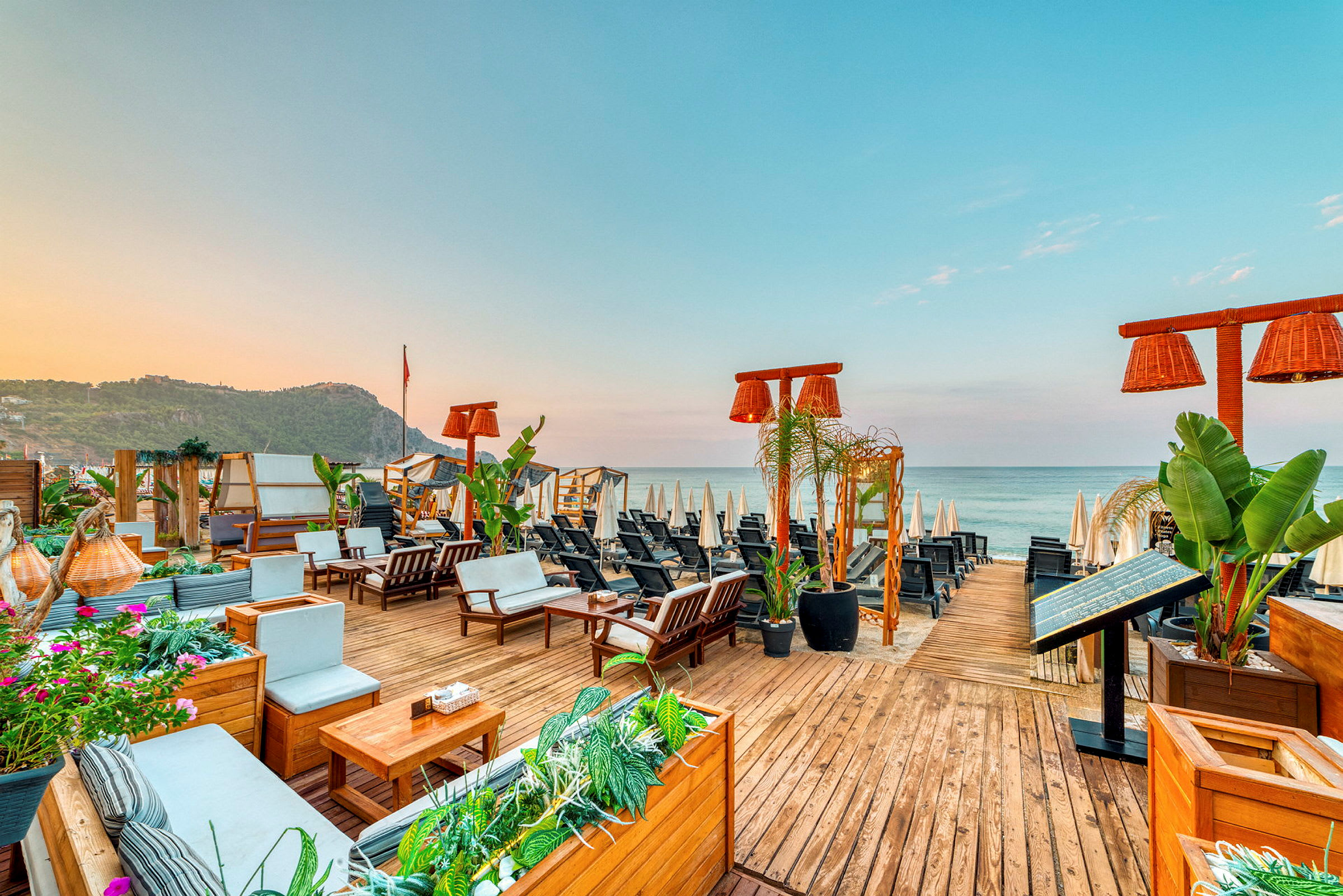 Udsigt over en strandbar med havemøbler og parasoller ved havet. (AI-genereret tekst)